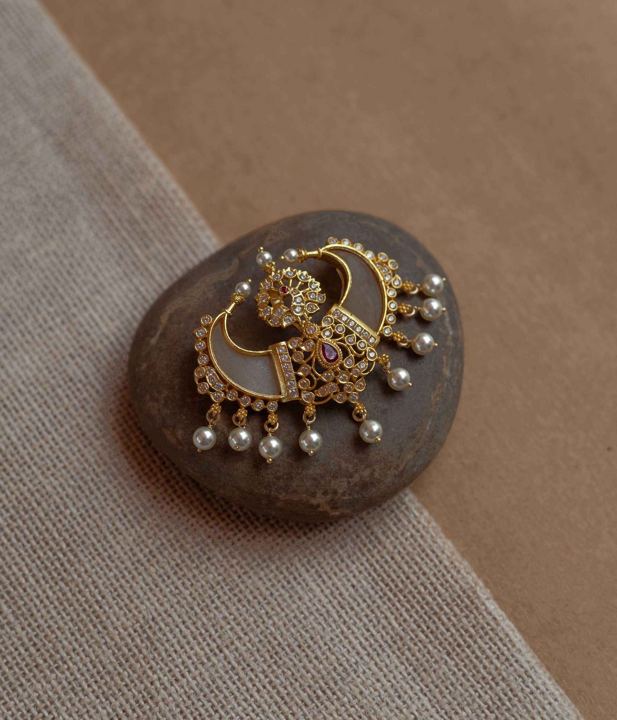 Gold pendant in twin crescent shape with CZ stones, pearls, and red spinal stone.