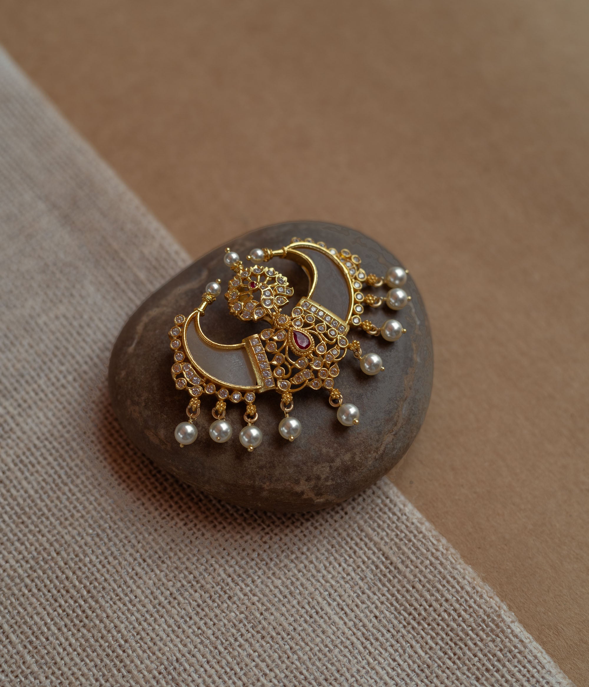 Gold pendant in twin crescent shape with CZ stones, pearls, and red spinal stone.
