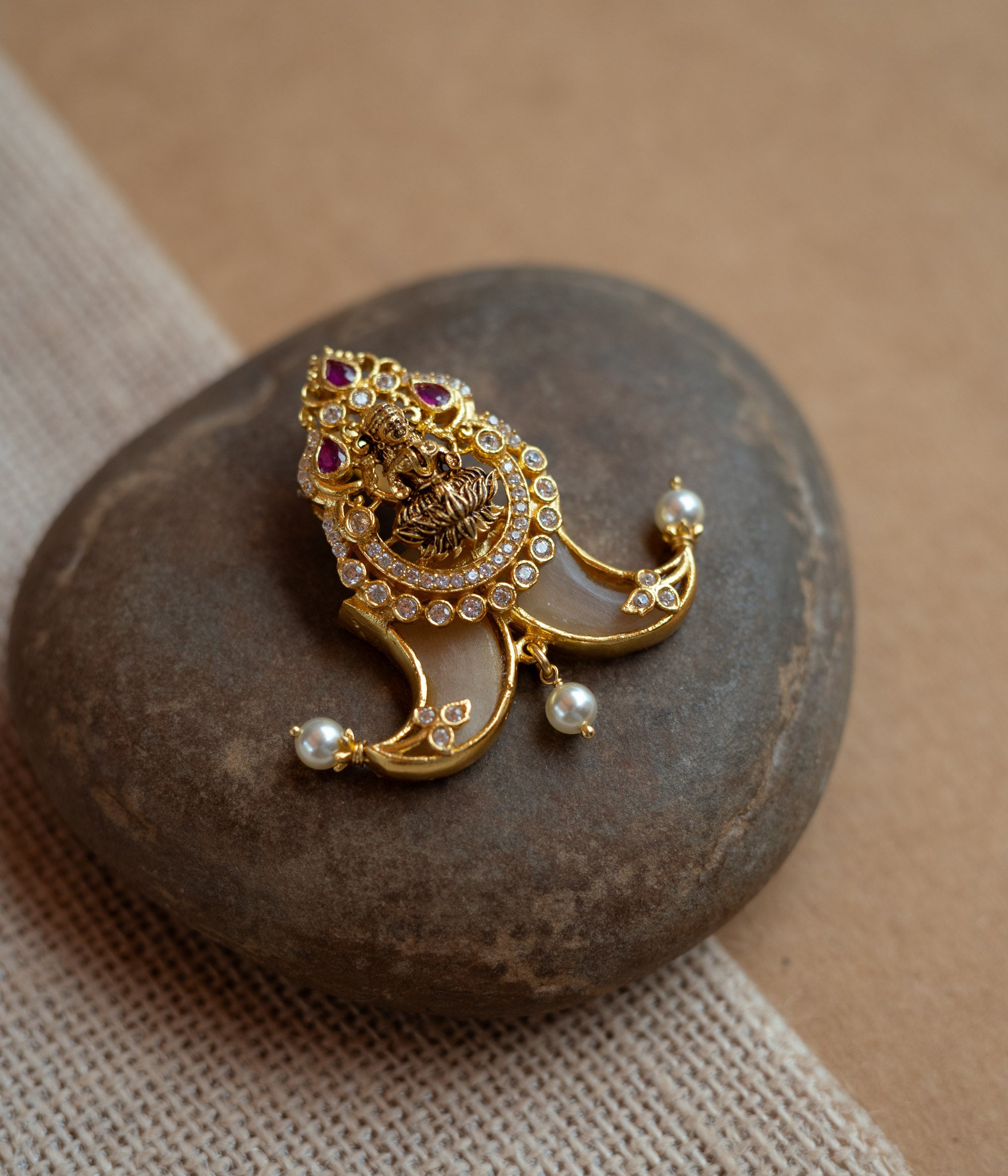 Gold amulet-shaped pendant with a goddess figure, red spinel, CZ stones, and pearls.