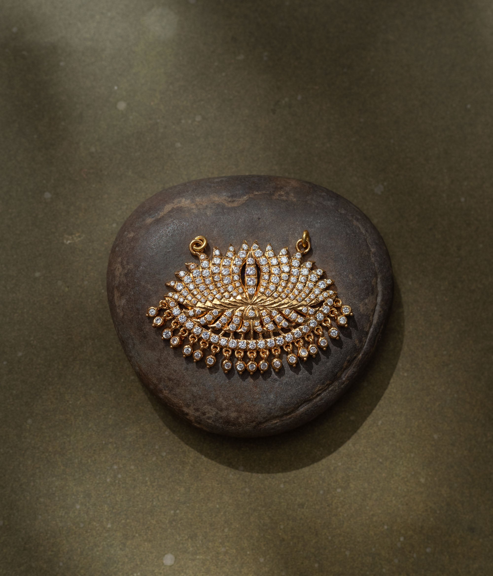 Gold fan-shaped pendant with CZ stones, inspired by peacock feather and sunburst motifs.
