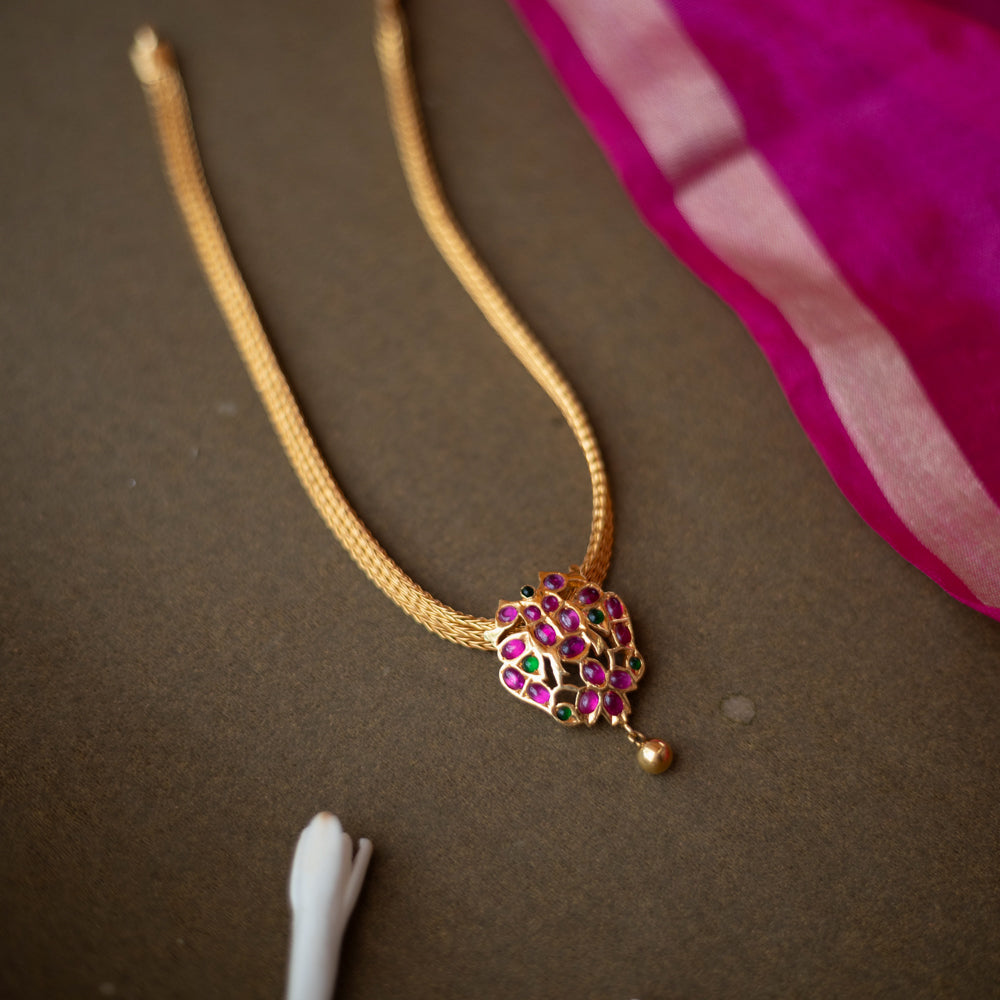 Gold-toned necklace with peacock-inspired pendant featuring red and green spinal stones.