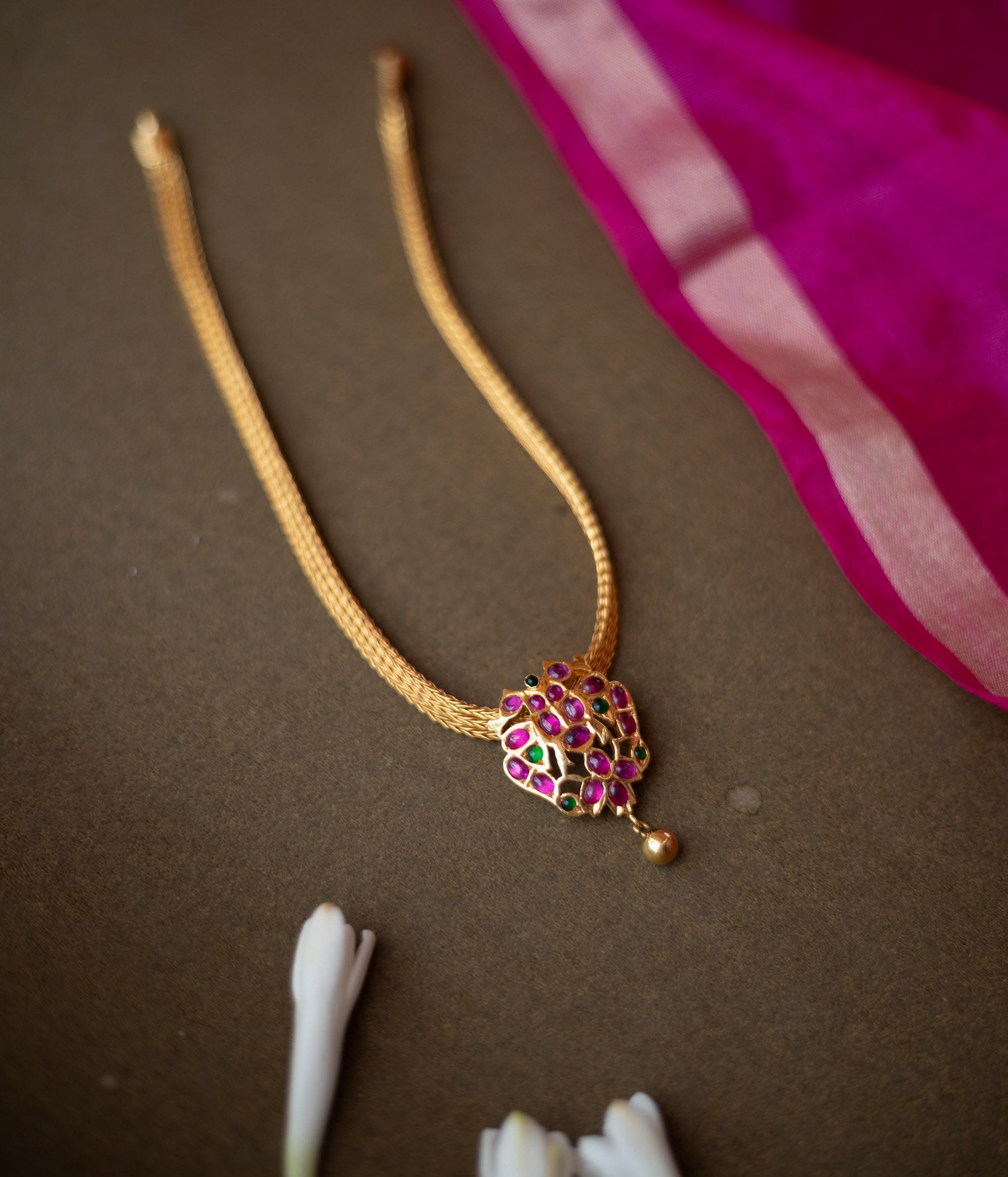 Gold-toned necklace with peacock-inspired pendant featuring red and green spinal stones.
