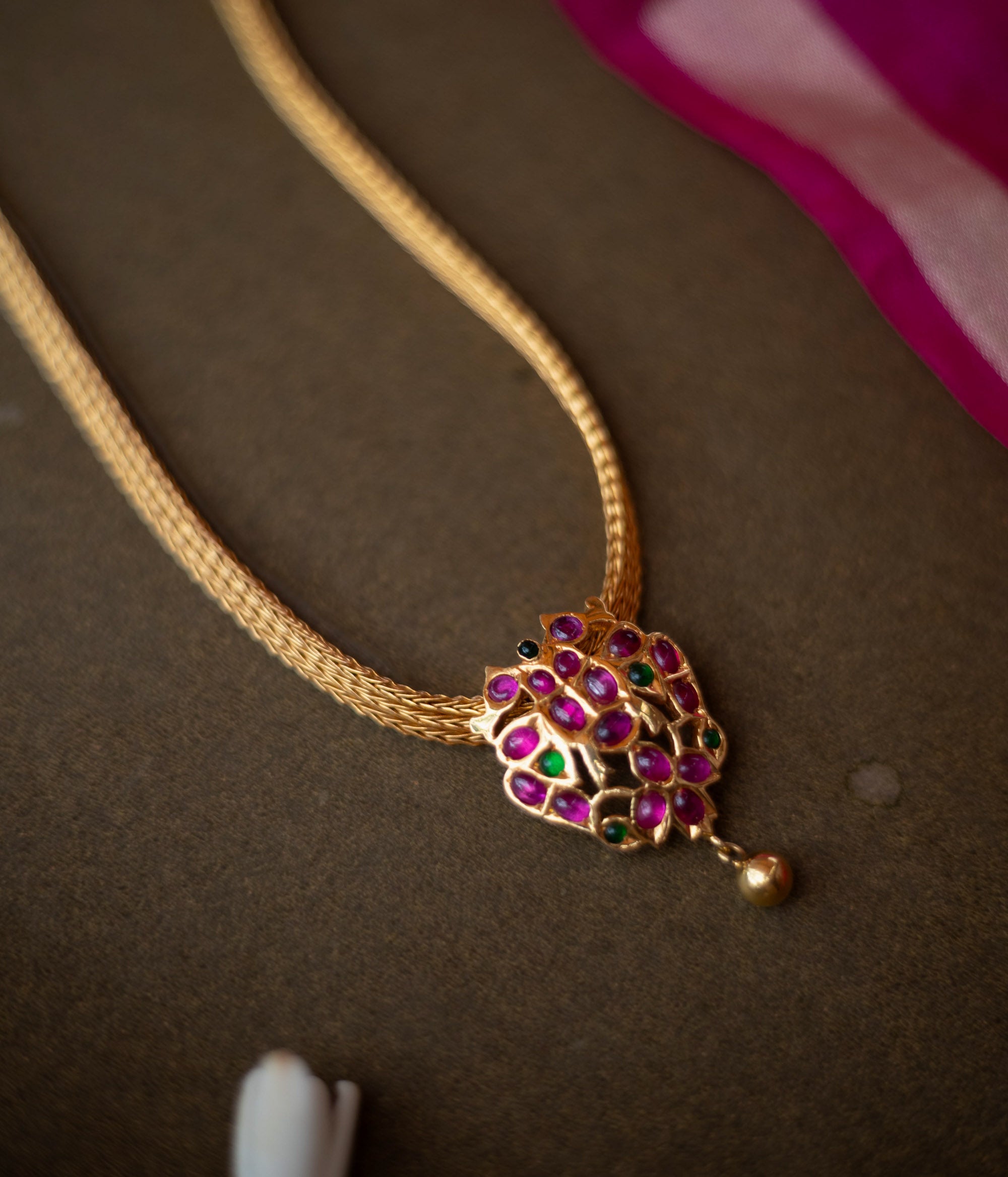 Gold-toned necklace with peacock-inspired pendant featuring red and green spinal stones.