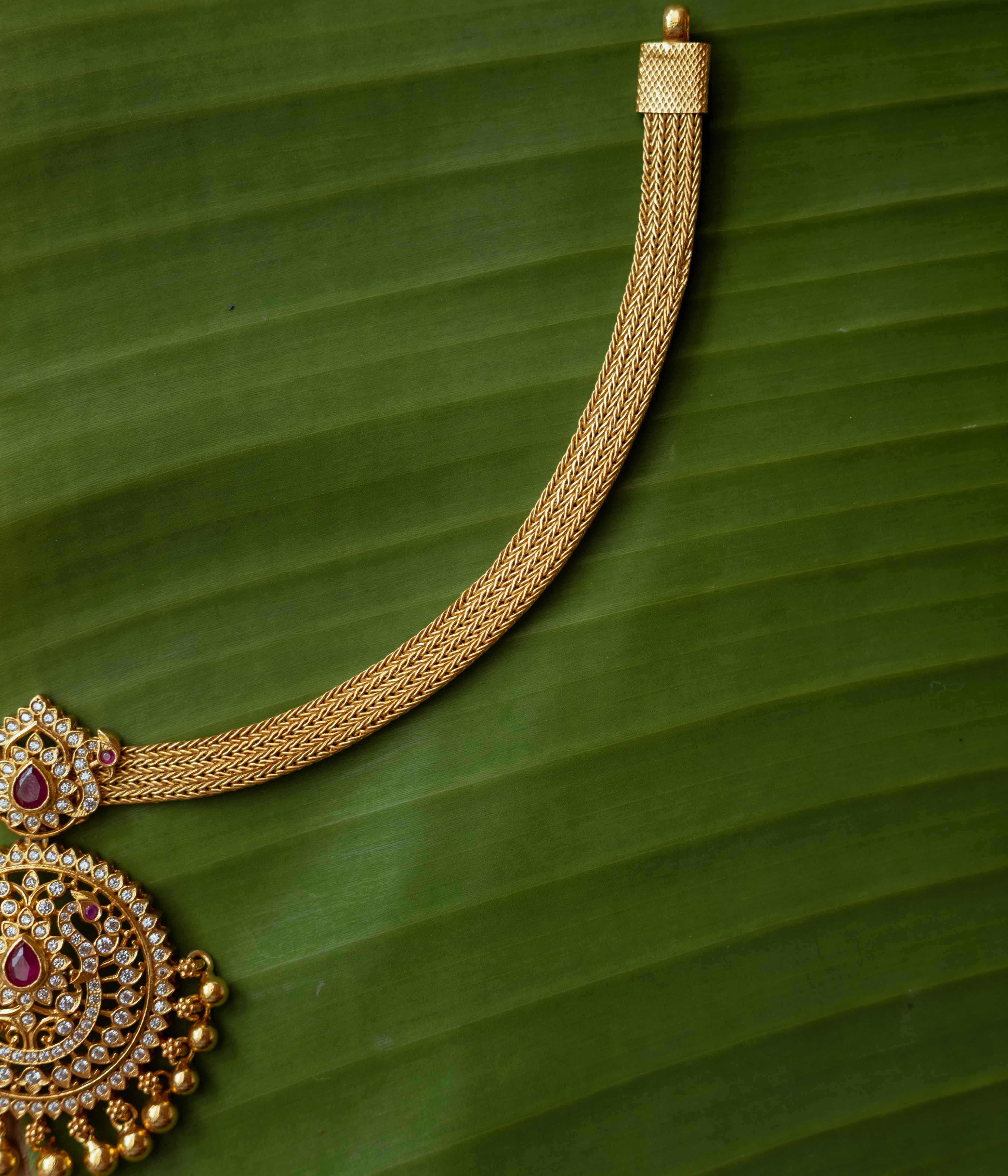 A necklace with a round pendant featuring a red stone, surrounded by clear stones, on a clear stone chain.
