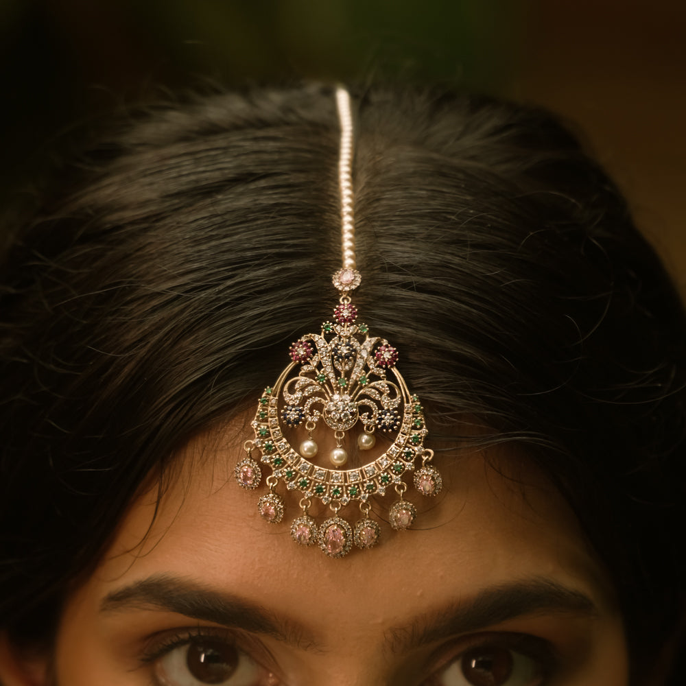 Traditional tikka with Swarovski stones, pink Kundan, and pearl drops in a floral crescent design.