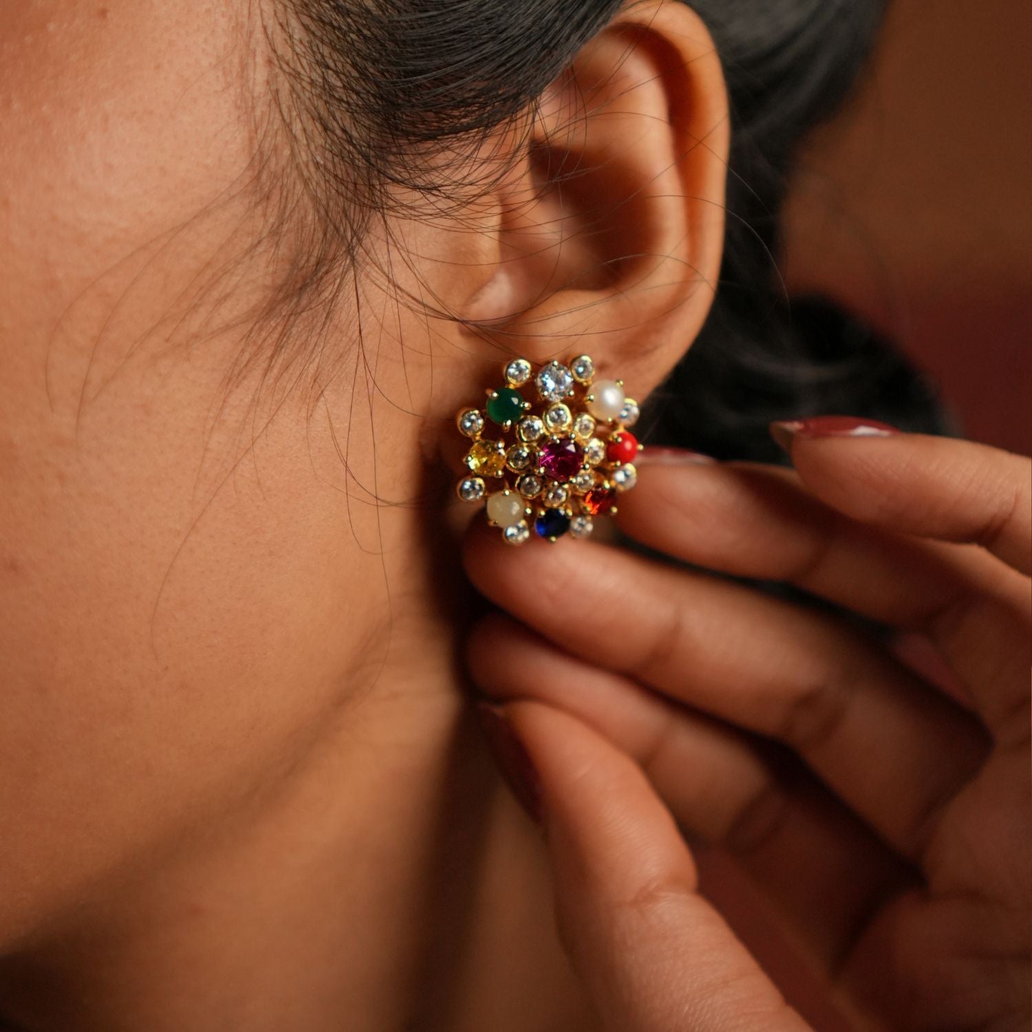 Navratna stud earrings bloom with celestial charm, each vibrant gemstone symbolizing cosmic energies and divine blessings in a timeless floral design.