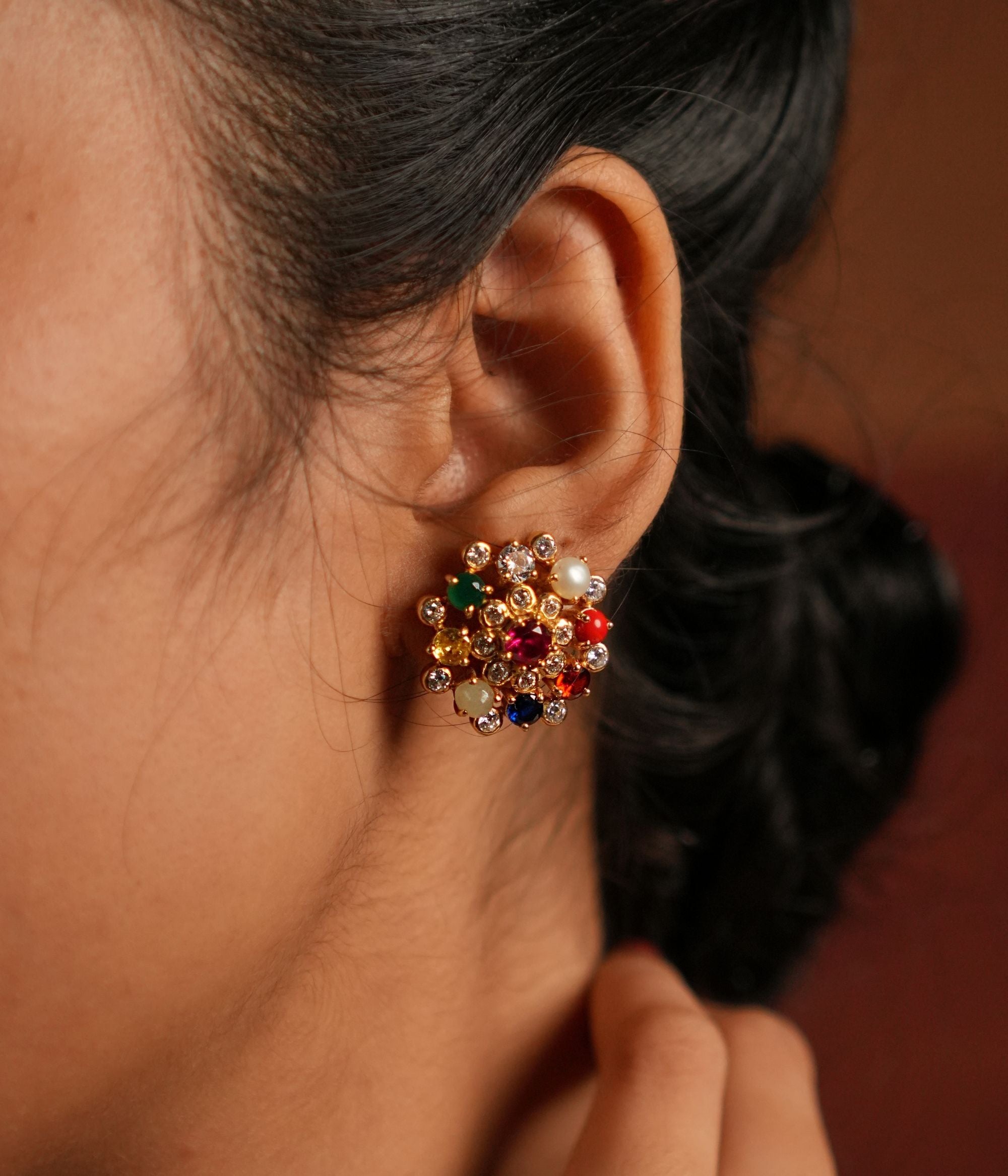 Navratna stud earrings bloom with celestial charm, each vibrant gemstone symbolizing cosmic energies and divine blessings in a timeless floral design.