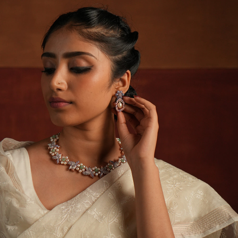 Exquisite drop earrings featuring a floral-shaped stud crafted from stunning tanzanite stones. The drop showcases an elegant asymmetrical design, encrusted with shimmering CZ stones and highlighted by a luminous pearl at the center, creating a sophisticated and timeless look.