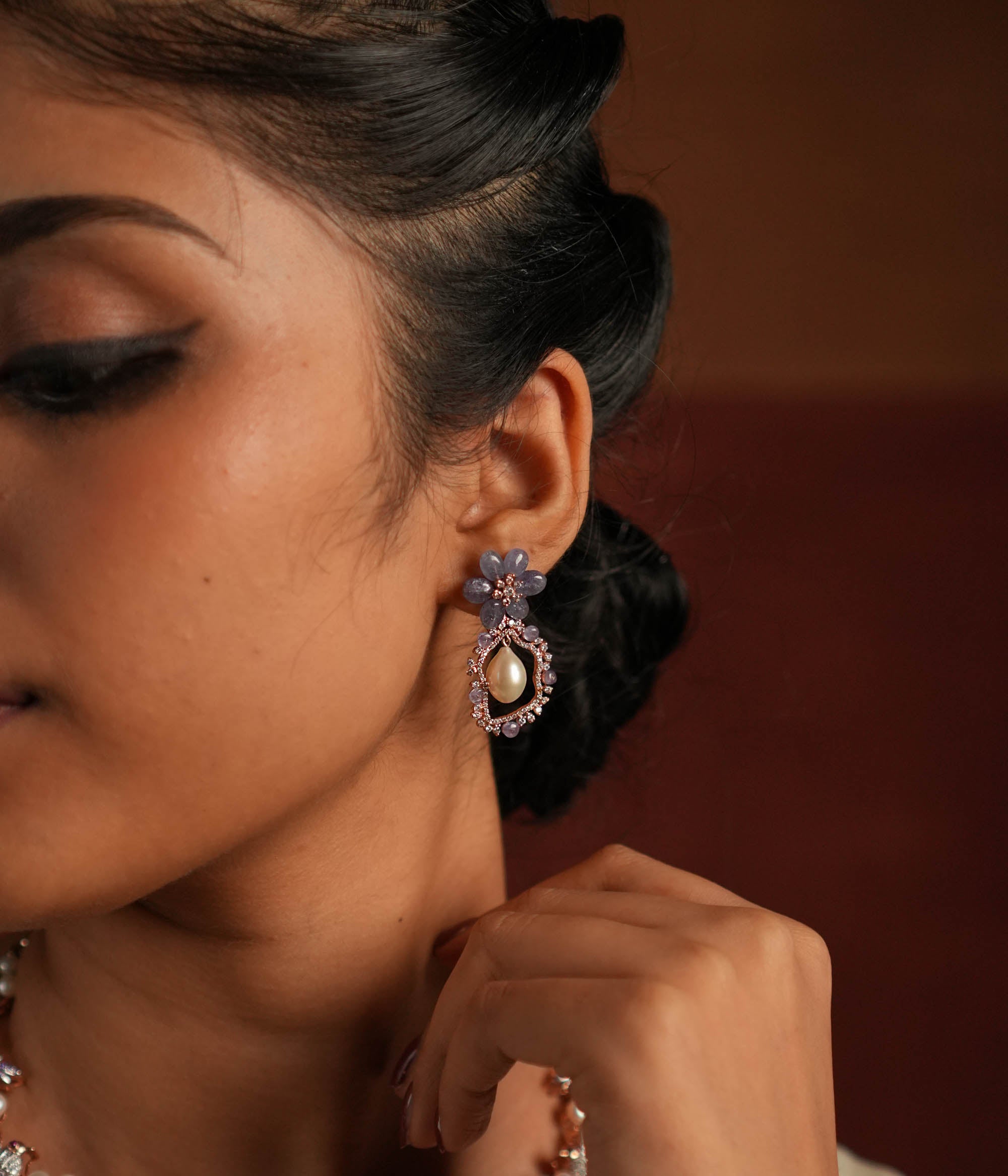 Exquisite drop earrings featuring a floral-shaped stud crafted from stunning tanzanite stones. The drop showcases an elegant asymmetrical design, encrusted with shimmering CZ stones and highlighted by a luminous pearl at the center, creating a sophisticated and timeless look.