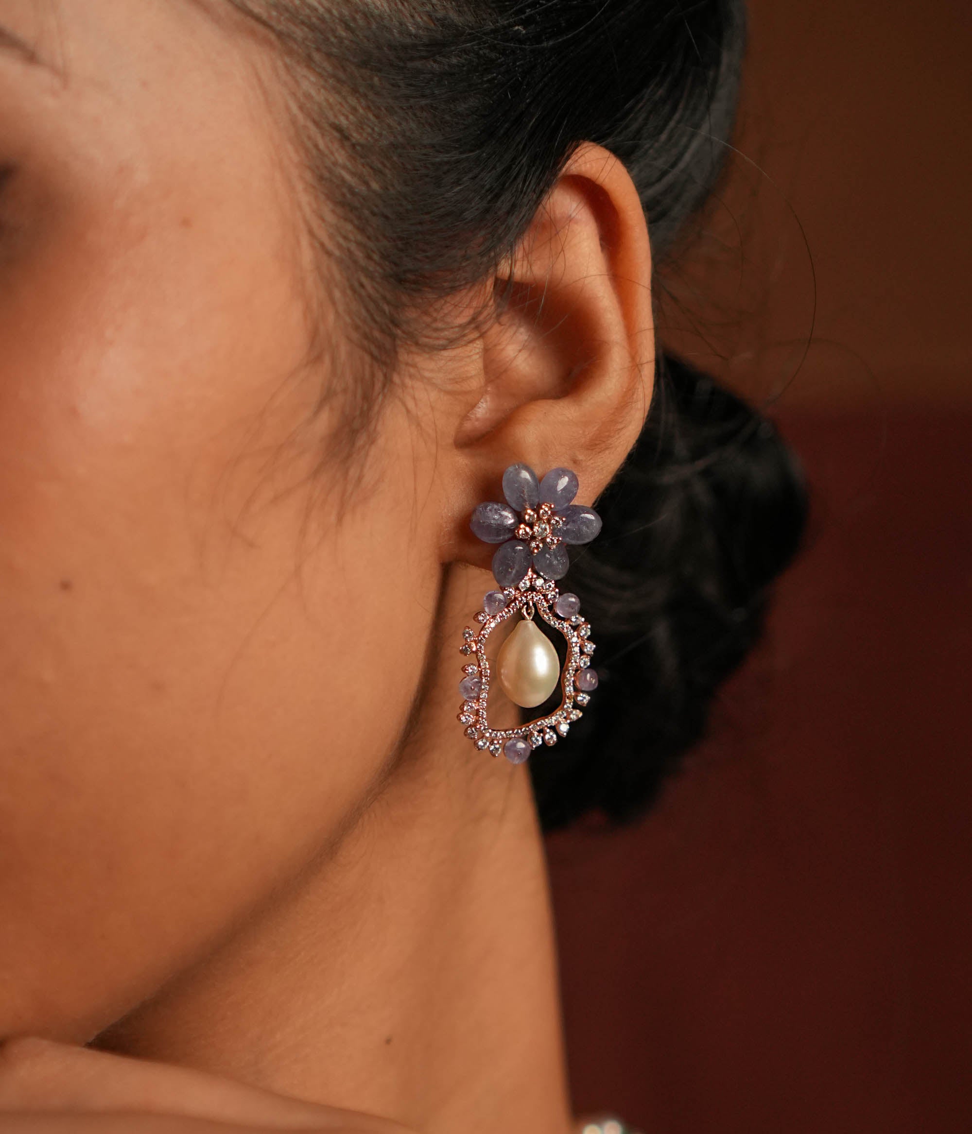 Exquisite drop earrings featuring a floral-shaped stud crafted from stunning tanzanite stones. The drop showcases an elegant asymmetrical design, encrusted with shimmering CZ stones and highlighted by a luminous pearl at the center, creating a sophisticated and timeless look.