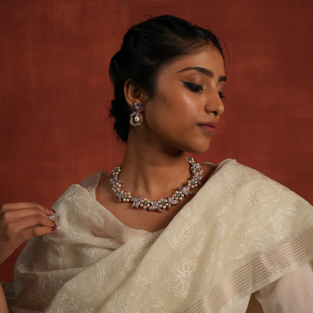 A stunning gold-plated silver necklace featuring an exquisite floral and bird design. The delicate flowers are crafted with lustrous pearls, while the intricately designed bird is adorned with shimmering CZ stones. The bird's eyes are highlighted with vibrant red spinel stones, adding a captivating touch. This elegant piece offers a unique and graceful finish, making it a timeless addition to any collection.