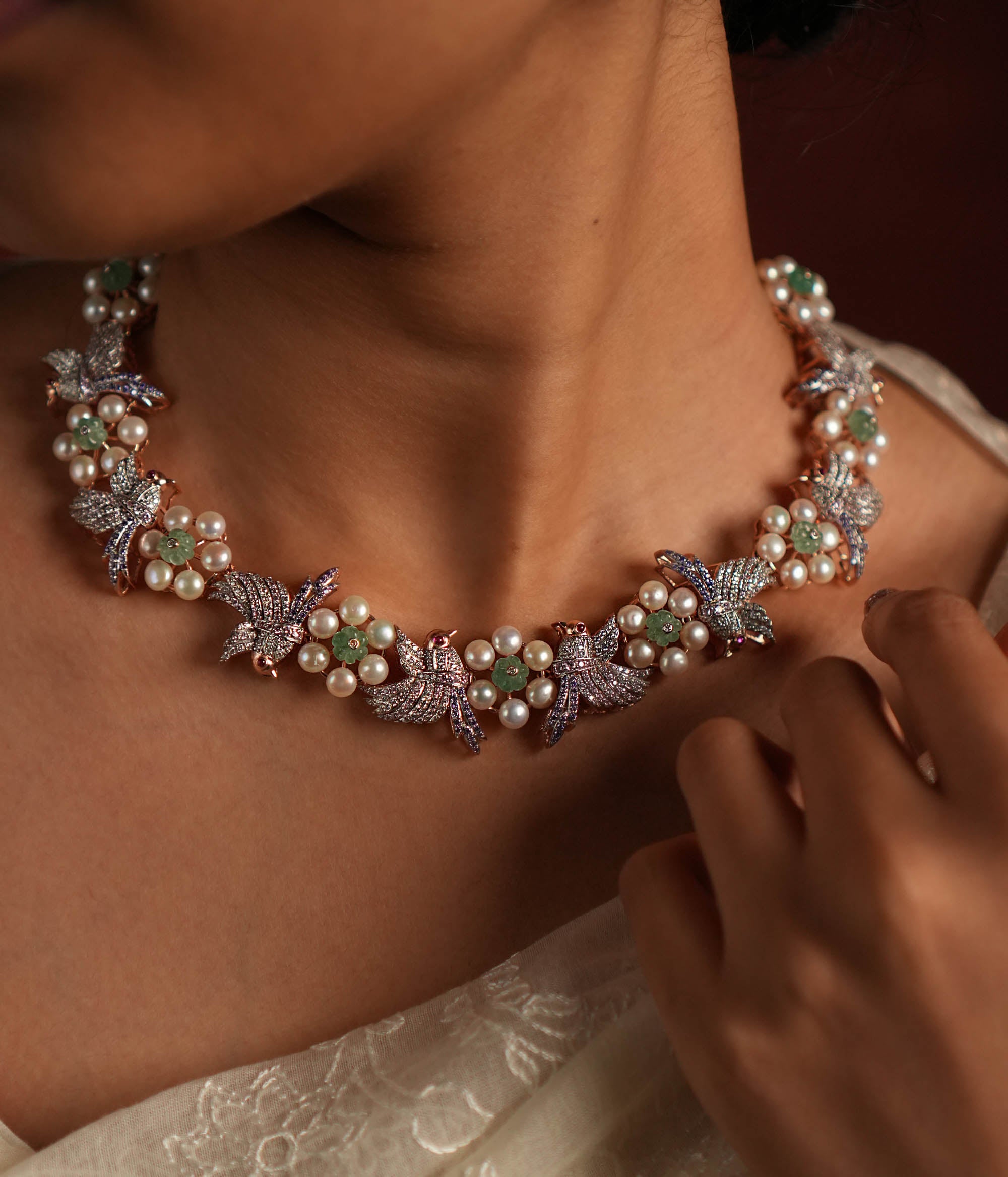 A stunning gold-plated silver necklace featuring an exquisite floral and bird design. The delicate flowers are crafted with lustrous pearls, while the intricately designed bird is adorned with shimmering CZ stones. The bird's eyes are highlighted with vibrant red spinel stones, adding a captivating touch. This elegant piece offers a unique and graceful finish, making it a timeless addition to any collection.
