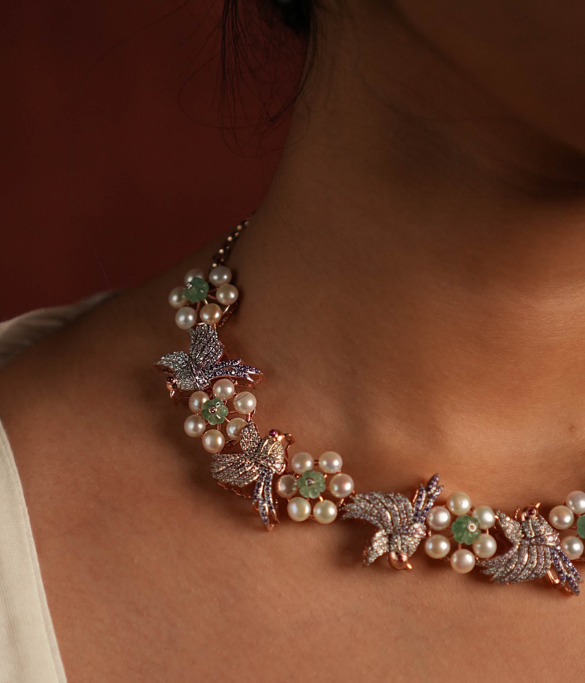 A stunning gold-plated silver necklace featuring an exquisite floral and bird design. The delicate flowers are crafted with lustrous pearls, while the intricately designed bird is adorned with shimmering CZ stones. The bird's eyes are highlighted with vibrant red spinel stones, adding a captivating touch. This elegant piece offers a unique and graceful finish, making it a timeless addition to any collection.
