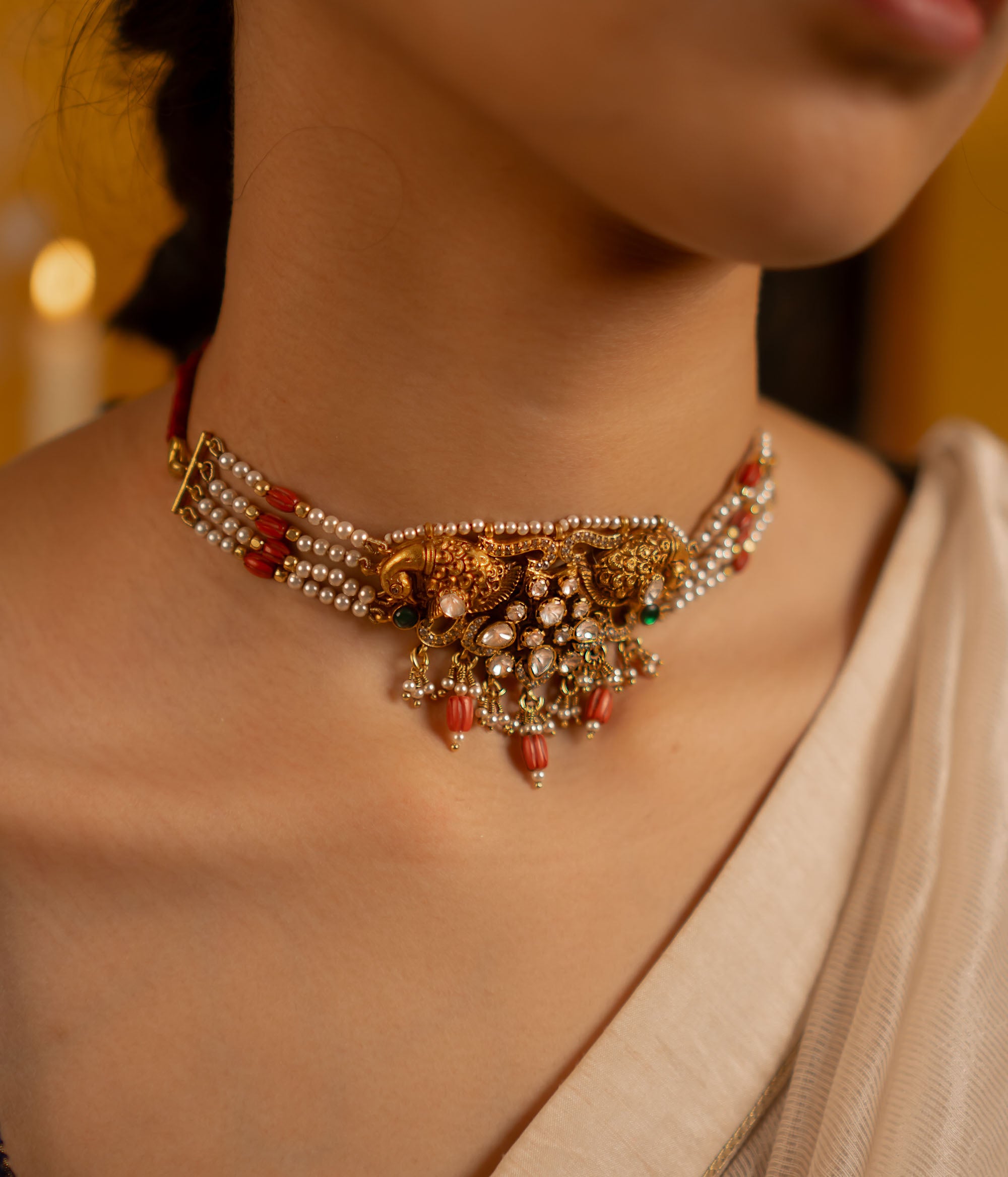This exquisite gold-plated silver choker showcases a stunning arrangement of red and green kundan stones, red beads, CZ stones, and pearls. Embellished with rose-cut polkis and graceful peacock motifs, it seamlessly fuses traditional artistry with modern elegance.