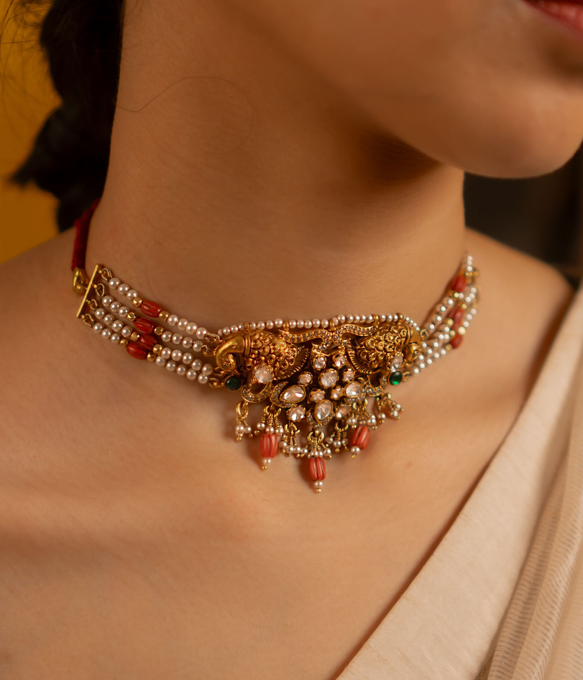 This exquisite gold-plated silver choker showcases a stunning arrangement of red and green kundan stones, red beads, CZ stones, and pearls. Embellished with rose-cut polkis and graceful peacock motifs, it seamlessly fuses traditional artistry with modern elegance.