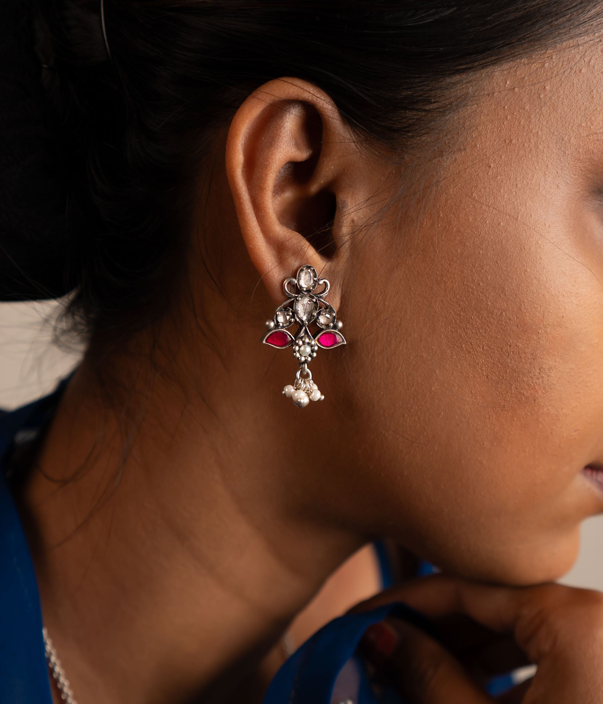 This oxidized silver drop earring features a stunning blend of red and white Kundan stones at its center, elegantly accented with freshwater pearl danglers for a timeless finish.