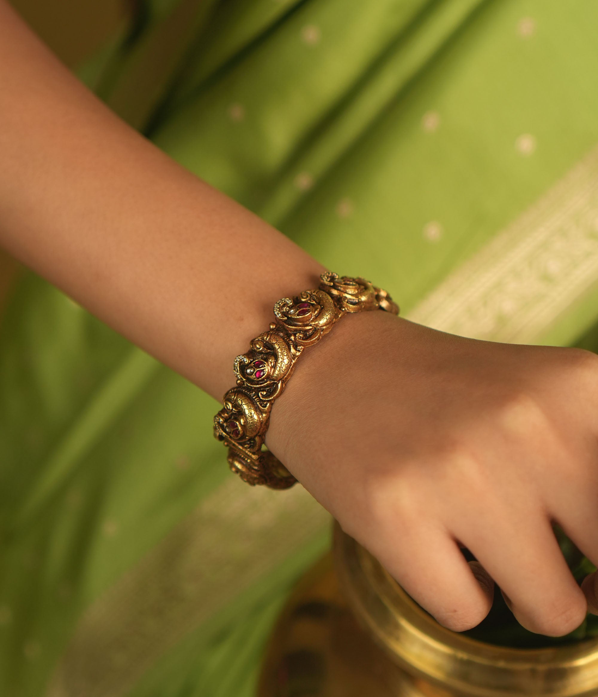 Embrace royal elegance with this stunning antique gold bangle, adorned with vibrant red, white, and green Kundan stones, featuring an intricate peacock motif. The regal peacock comes to life in this piece, while the pink Kundan hues add a touch of grandeur. A perfect fusion of heritage and artistry, this bangle exudes timeless splendor.