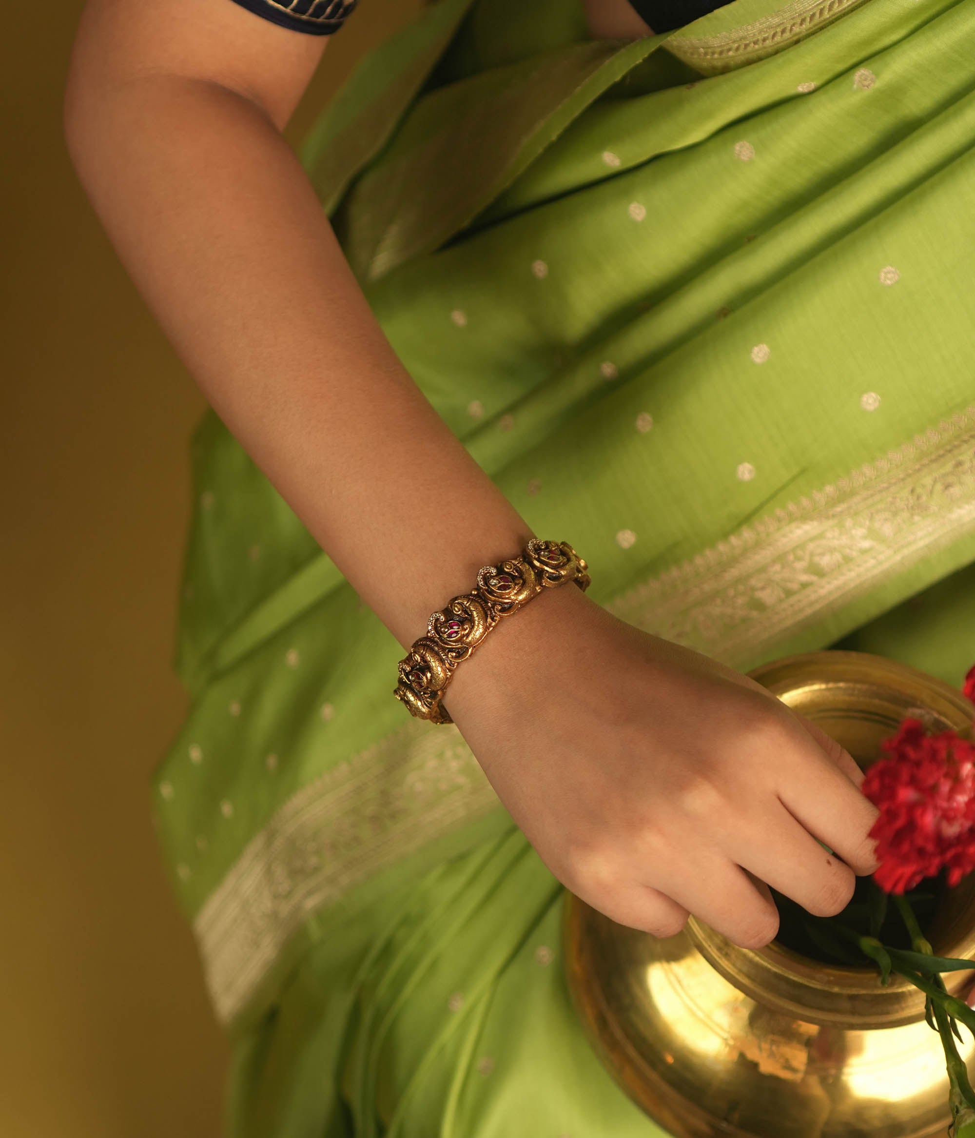 Embrace royal elegance with this stunning antique gold bangle, adorned with vibrant red, white, and green Kundan stones, featuring an intricate peacock motif. The regal peacock comes to life in this piece, while the pink Kundan hues add a touch of grandeur. A perfect fusion of heritage and artistry, this bangle exudes timeless splendor.