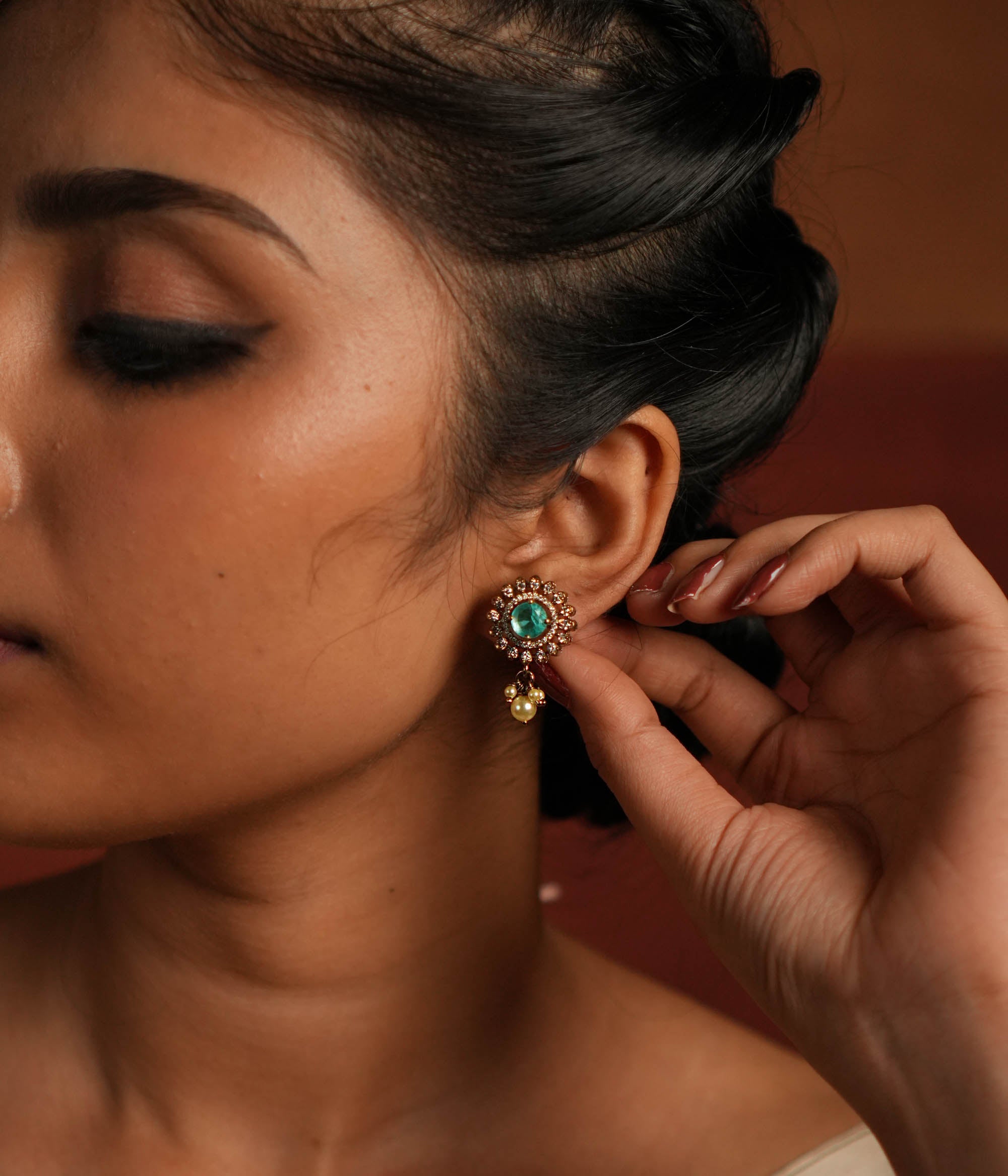 Elegant gold-plated silver drop earrings featuring a round design with a striking green spinel stone at the center, encased in multiple layers of shimmering CZ stones. The exquisite drop is adorned with delicate pearls, adding a touch of grace and sophistication. A perfect blend of tradition and elegance, these earrings make a timeless statement.