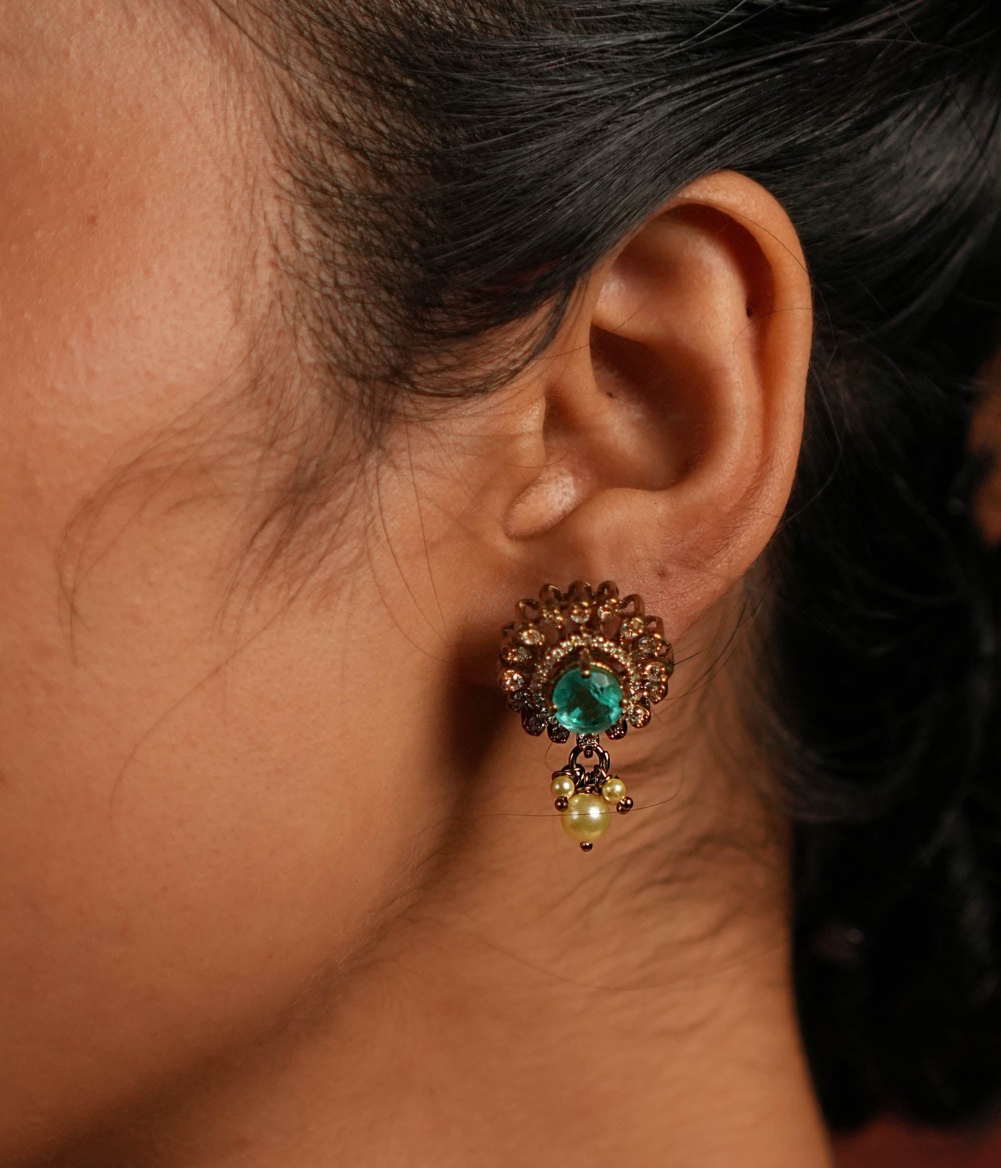 Elegant gold-plated silver drop earrings featuring a round design with a striking green spinel stone at the center, encased in multiple layers of shimmering CZ stones. The exquisite drop is adorned with delicate pearls, adding a touch of grace and sophistication. A perfect blend of tradition and elegance, these earrings make a timeless statement.