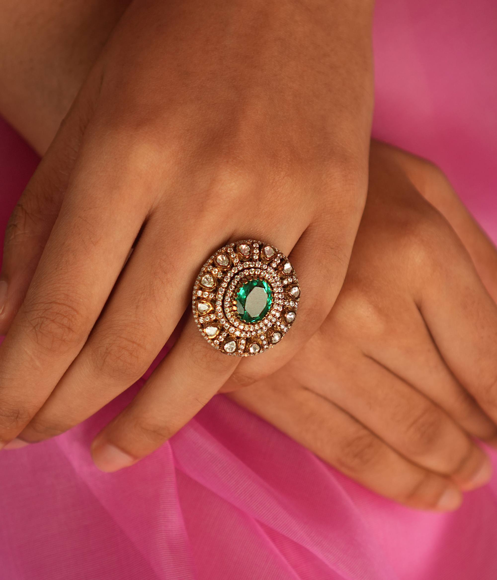 A Victorian-inspired Moissanite ring, featuring a mesmerizing green gemstone at its heart, radiates timeless elegance and sophistication with its halo of polki and CZ stones.