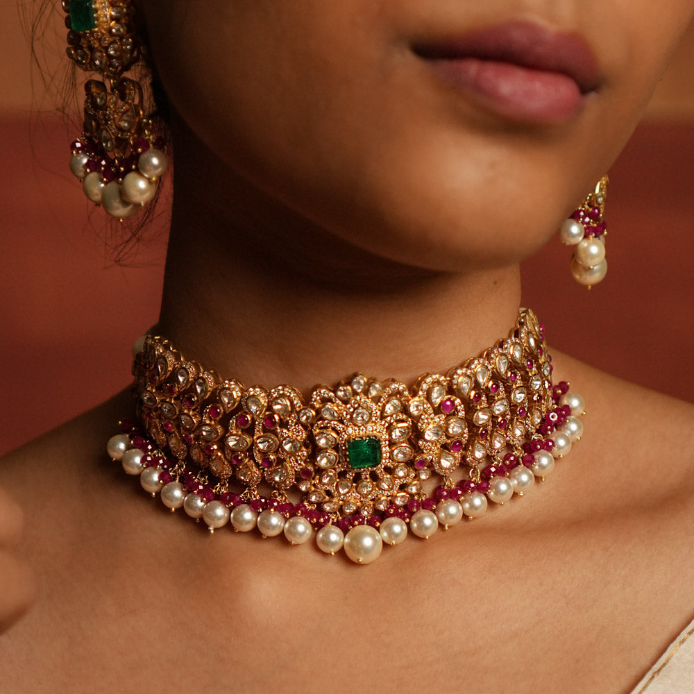 Exquisite choker featuring a central floral design adorned with Green Gemstone, Moissanite Polki Stones, Red Beads, Pearls, and CZ Stones. The choker showcases a continuous chain of Polki and Red Beads, elegantly finished with delicate pearl drops for a regal look.