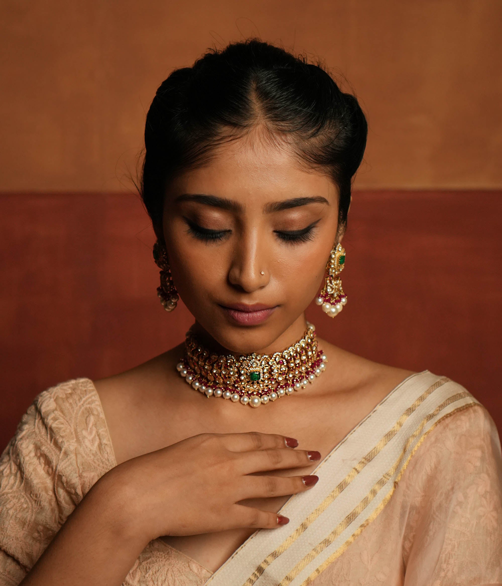 Exquisite choker featuring a central floral design adorned with Green Gemstone, Moissanite Polki Stones, Red Beads, Pearls, and CZ Stones. The choker showcases a continuous chain of Polki and Red Beads, elegantly finished with delicate pearl drops for a regal look.