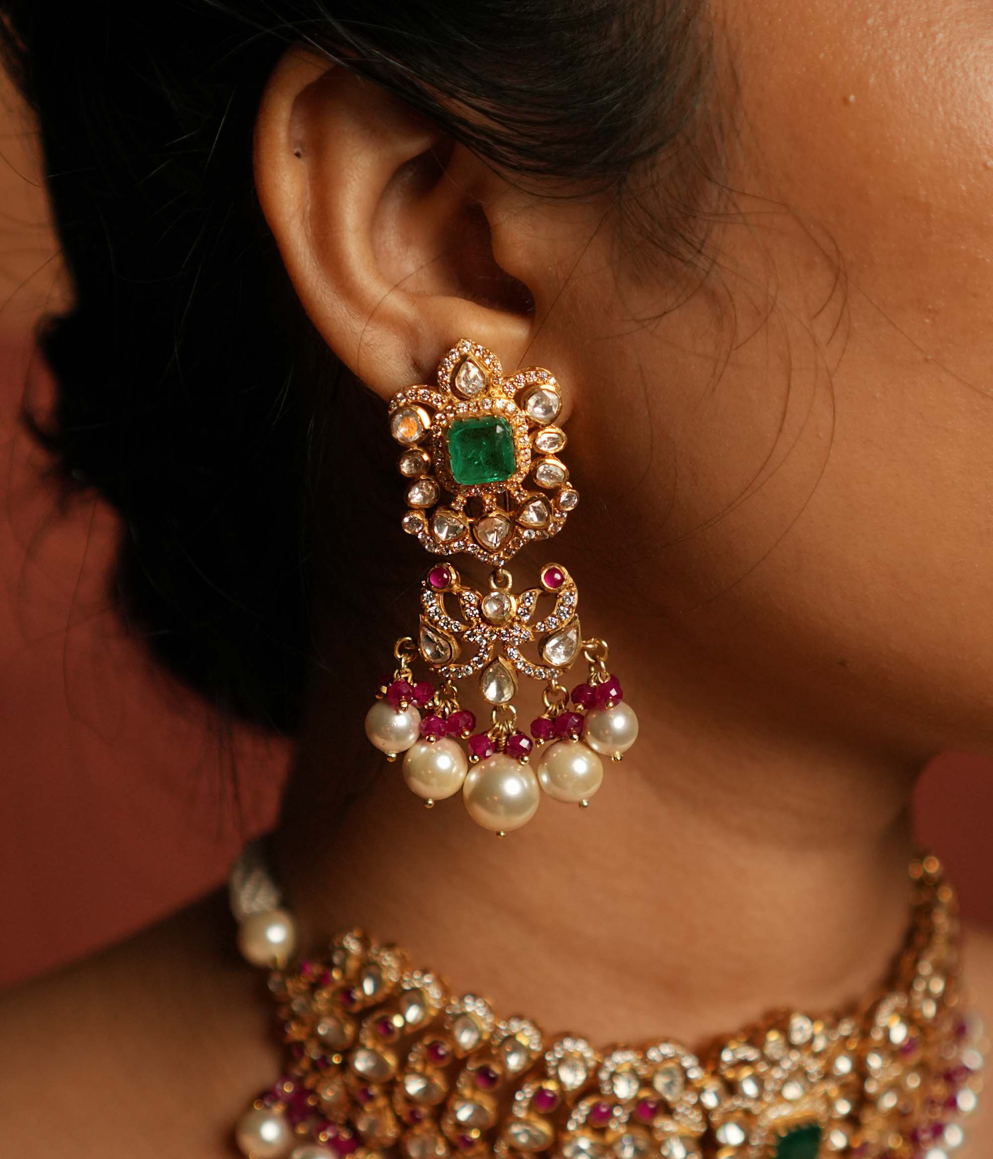Elegant dangler earrings featuring a floral design adorned with Green Gemstone, Moissanite Polki Stones, Red Beads, Pearls, and CZ Stones. The earrings showcase a continuous arrangement of Polki and Red Beads, gracefully finished with delicate pearl drops for a sophisticated look.