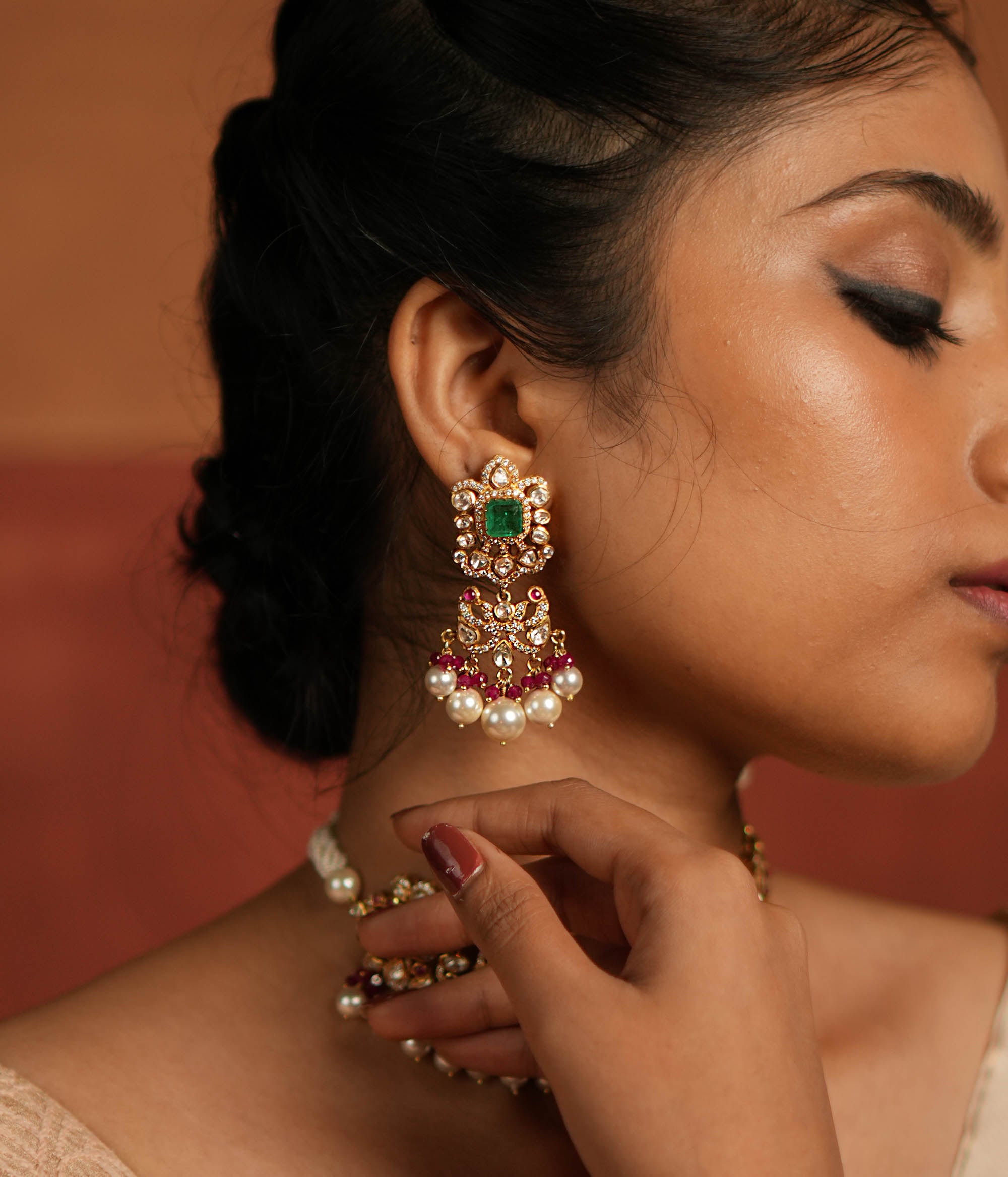 Elegant dangler earrings featuring a floral design adorned with Green Gemstone, Moissanite Polki Stones, Red Beads, Pearls, and CZ Stones. The earrings showcase a continuous arrangement of Polki and Red Beads, gracefully finished with delicate pearl drops for a sophisticated look.