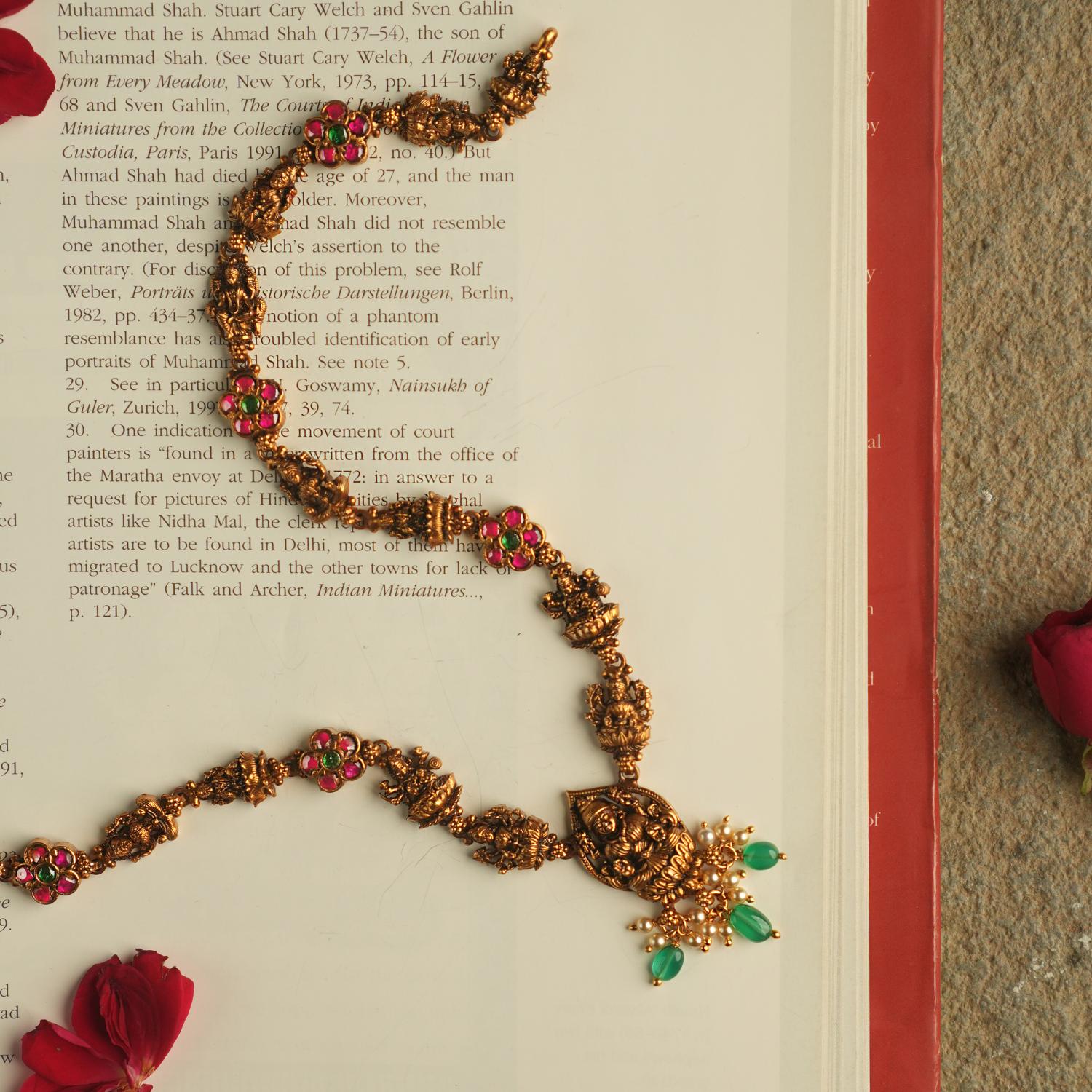 The Aadhya necklace evokes the charm of a bygone era, with antique gold, polkis, and a divine Lakshmi pendant. Pearl drops and green beads add a touch of timeless grace.