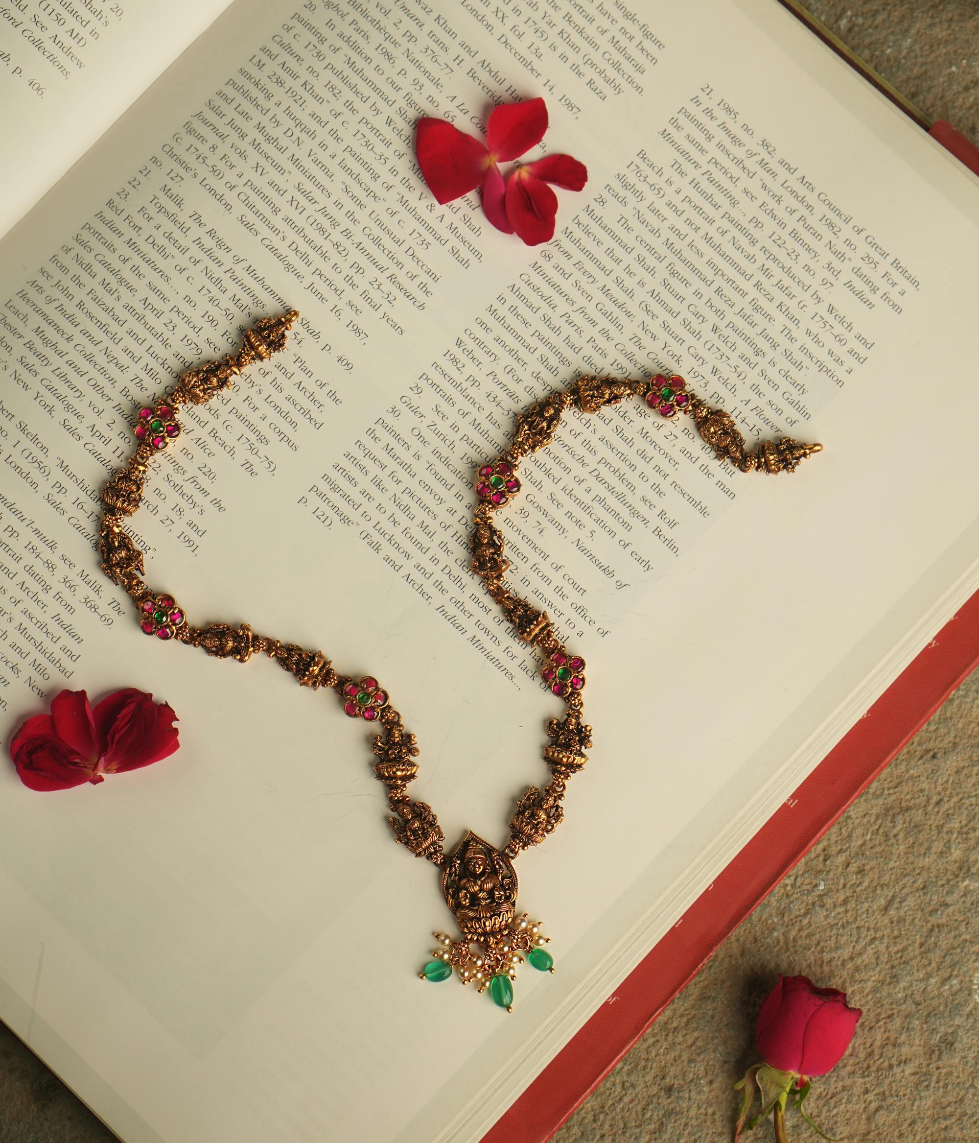 The Aadhya necklace evokes the charm of a bygone era, with antique gold, polkis, and a divine Lakshmi pendant. Pearl drops and green beads add a touch of timeless grace.