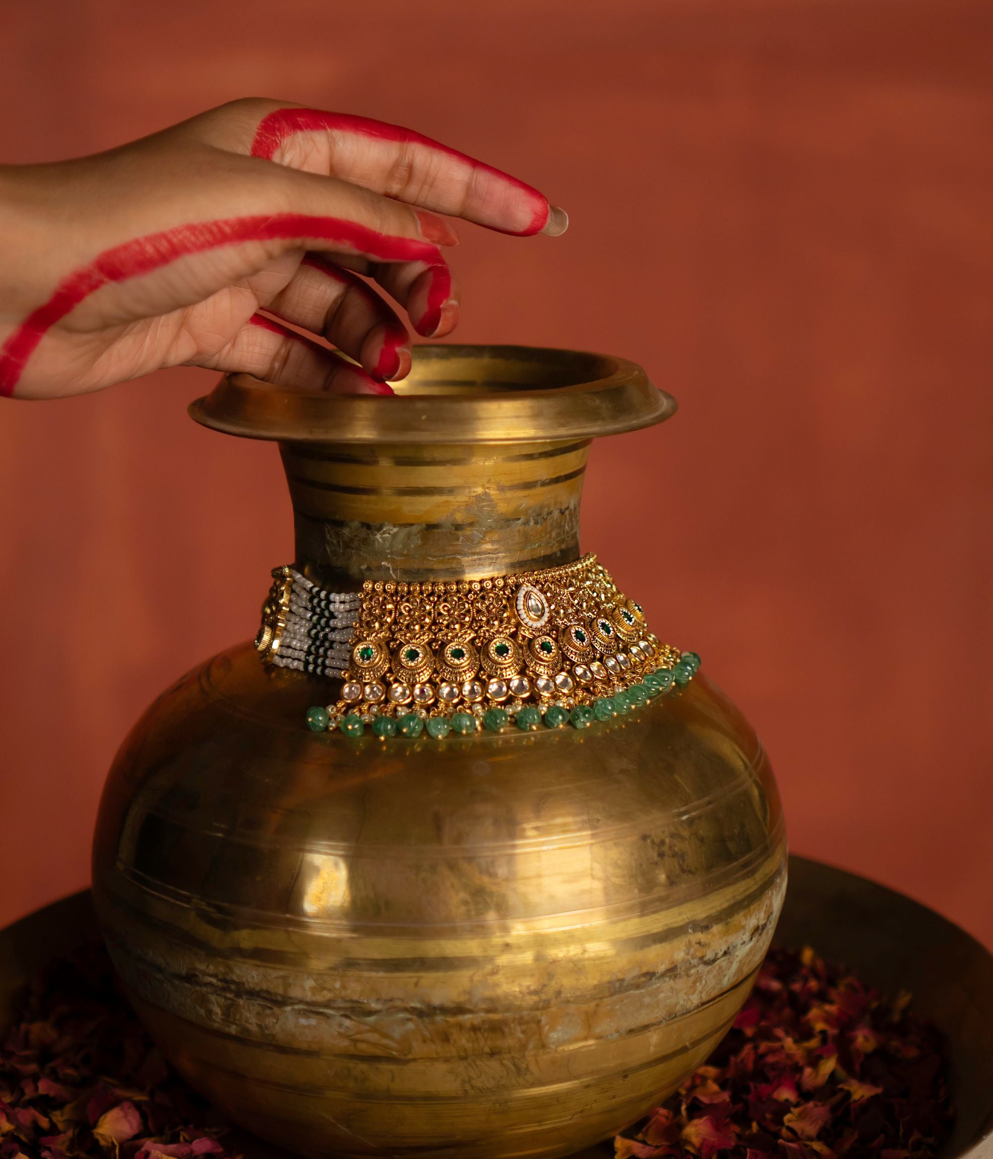 A gold necklace, richly embellished with white, green, and gold accents, is artfully draped over a vintage-style brass pot. The ornate necklace, with its intricate detailing, contrasts beautifully with the rustic texture of the pot. This juxtaposition highlights the craftsmanship of the necklace and creates a visually compelling composition.