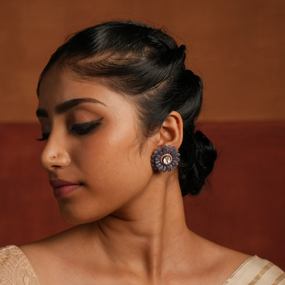 A stunning gold-plated silver stud earring in an elegant flower shape, beautifully crafted with exquisite Tanzanite stones. The center features a dazzling Polki stone, encircled by shimmering CZ stones, adding a touch of brilliance. This timeless design blends sophistication and charm, making it a perfect accessory for any occasion.