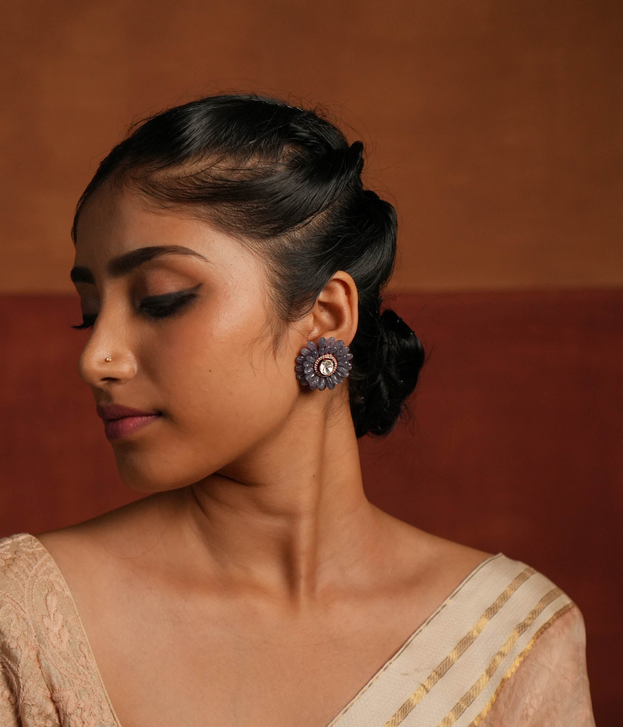 A stunning gold-plated silver stud earring in an elegant flower shape, beautifully crafted with exquisite Tanzanite stones. The center features a dazzling Polki stone, encircled by shimmering CZ stones, adding a touch of brilliance. This timeless design blends sophistication and charm, making it a perfect accessory for any occasion.