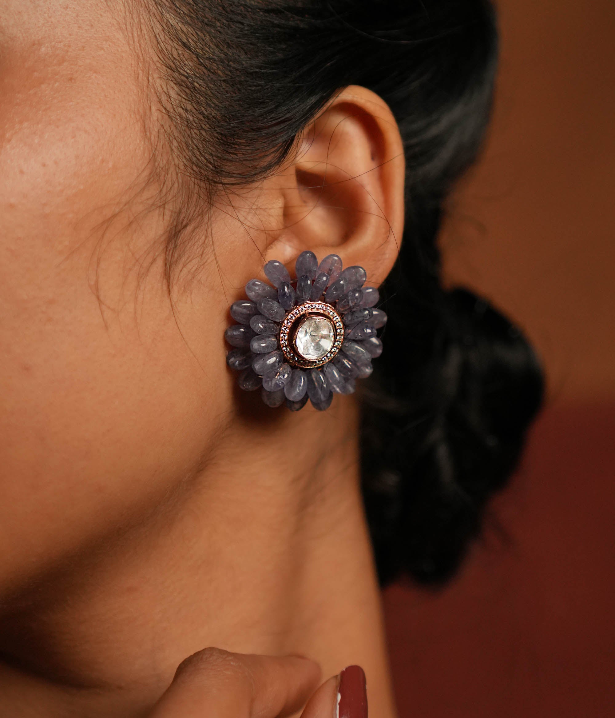 A stunning gold-plated silver stud earring in an elegant flower shape, beautifully crafted with exquisite Tanzanite stones. The center features a dazzling Polki stone, encircled by shimmering CZ stones, adding a touch of brilliance. This timeless design blends sophistication and charm, making it a perfect accessory for any occasion.