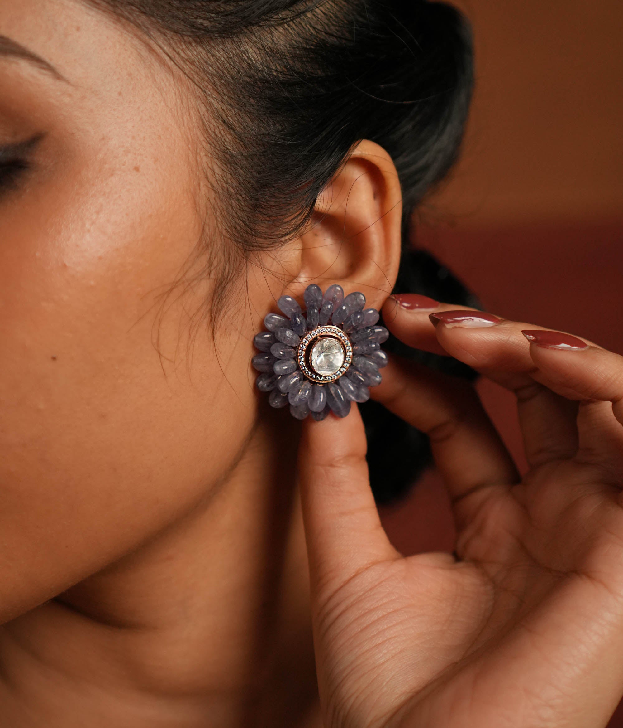A stunning gold-plated silver stud earring in an elegant flower shape, beautifully crafted with exquisite Tanzanite stones. The center features a dazzling Polki stone, encircled by shimmering CZ stones, adding a touch of brilliance. This timeless design blends sophistication and charm, making it a perfect accessory for any occasion.