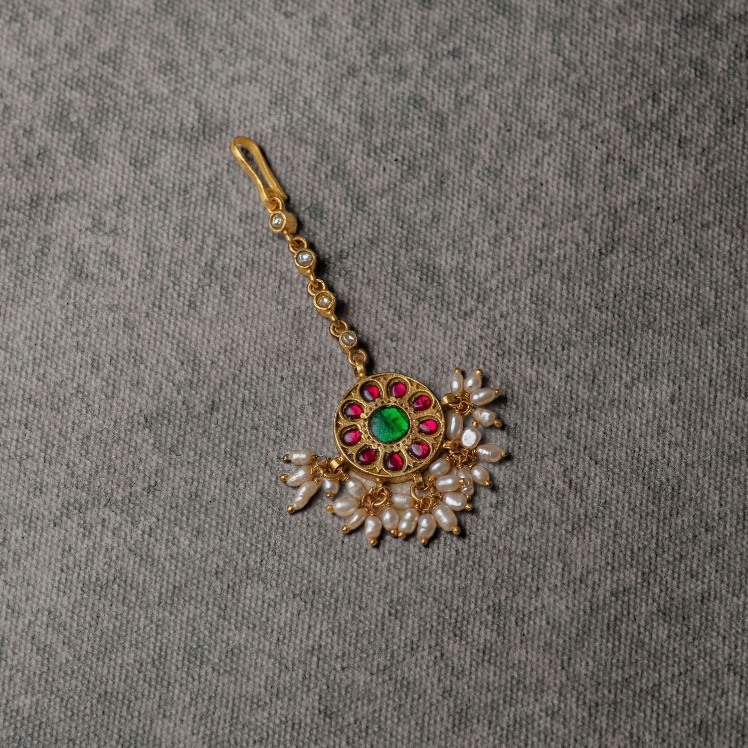 A cherished heirloom, this antique-inspired tikka features red and green Kundan stones with white pearls, embodying elegance and tradition through its timeless craftsmanship.