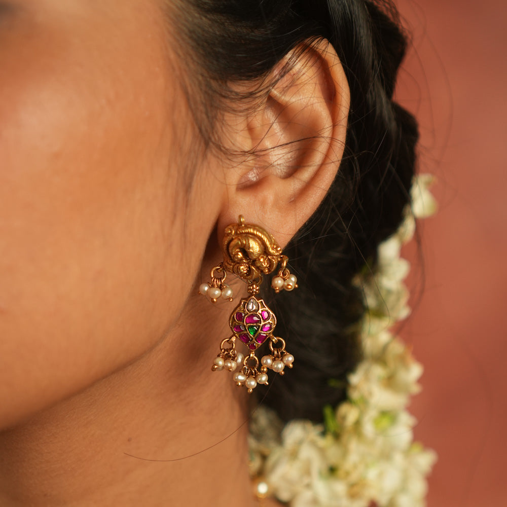 Bazaar whispers reborn! Kundan peacock dangler earrings with pearl droplets dance in harmony with vibrant gems, crafting a symphony of elegance.