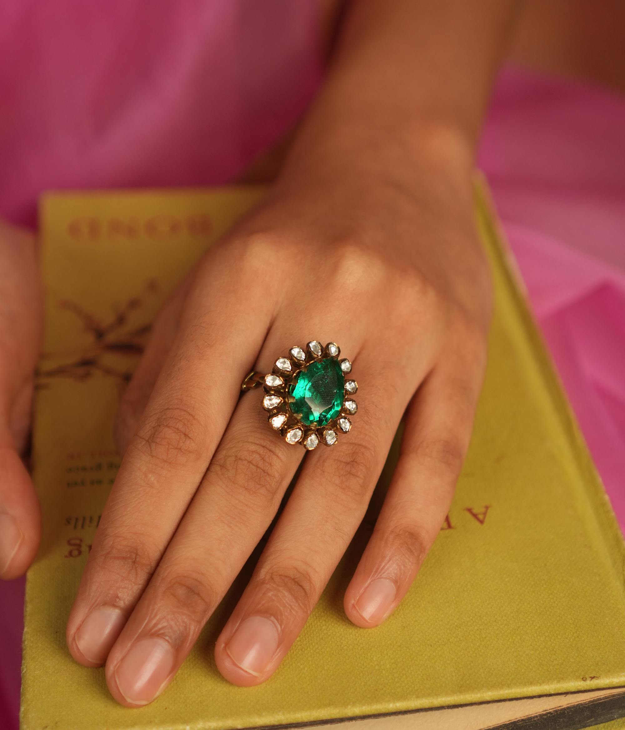 A teardrop ring featuring a vivid green gemstone, encircled by shimmering Polki and CZ stones, where each facet sparkles with celestial brilliance, echoing timeless elegance.