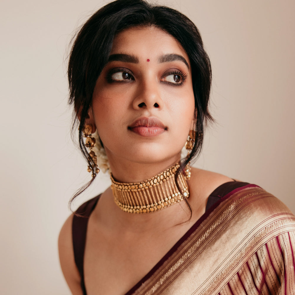 Bold tribal gold choker with vertical bar design and bead detailing, worn with maroon saree.