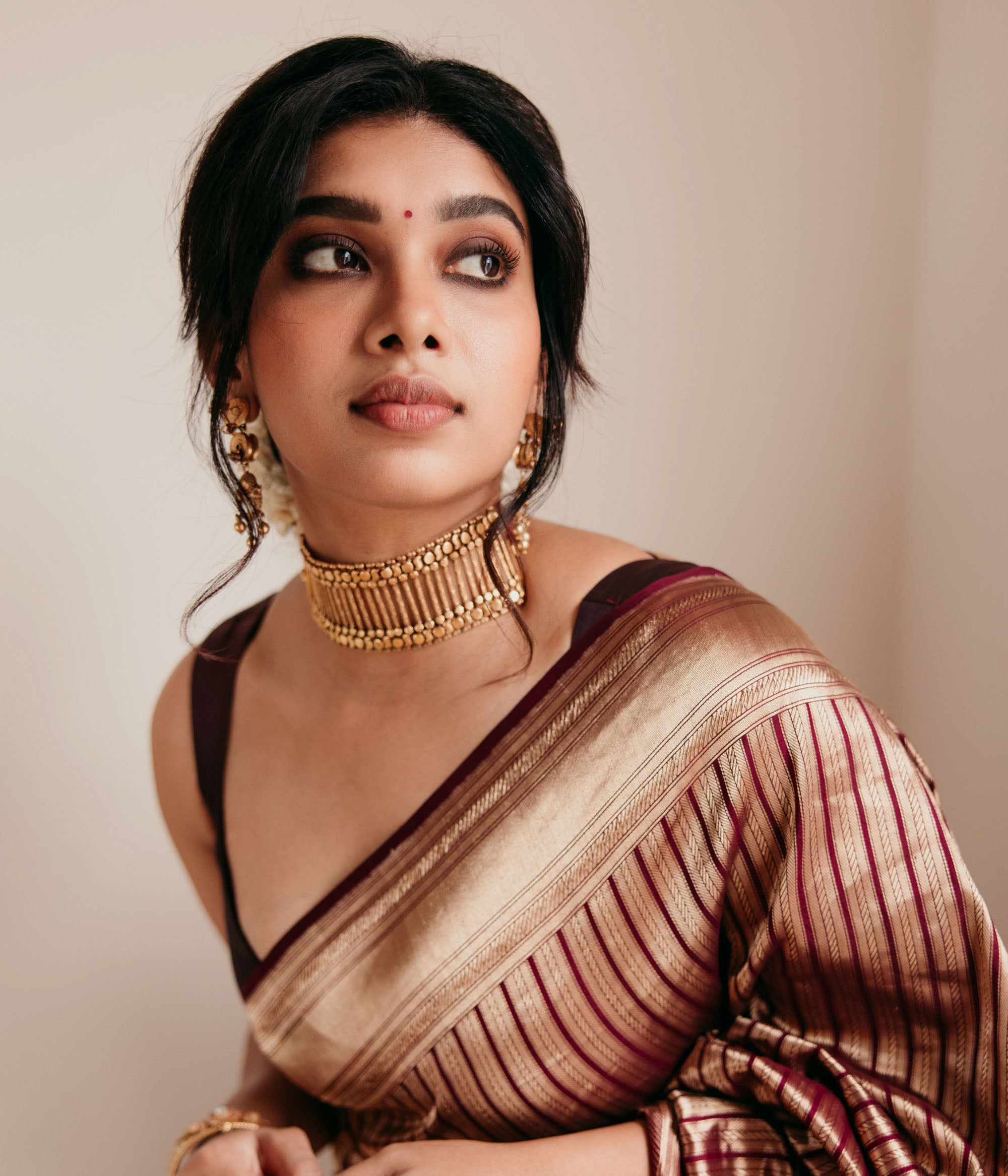 Bold tribal gold choker with vertical bar design and bead detailing, worn with maroon saree.