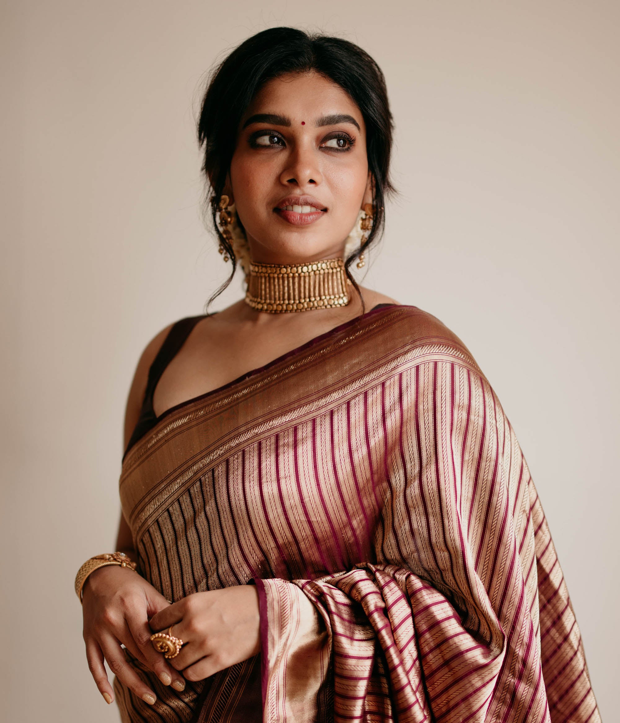 Bold tribal gold choker with vertical bar design and bead detailing, worn with maroon saree.