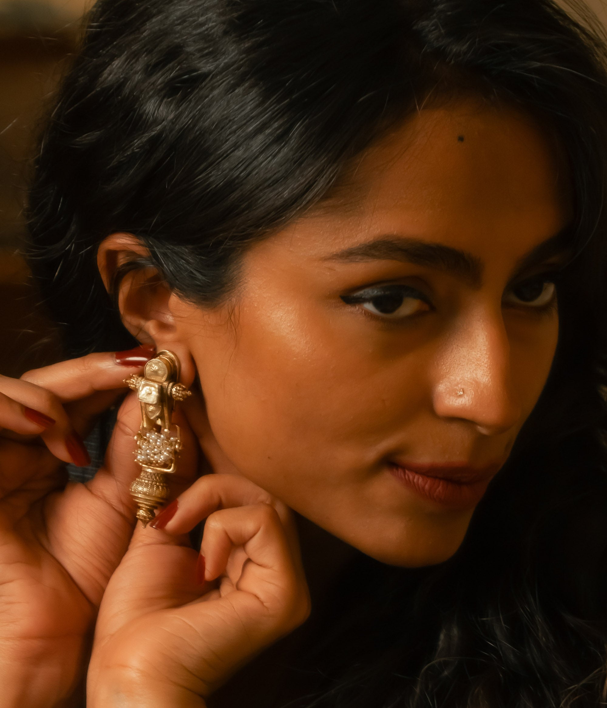 Long gold tribal dangle earrings with white polki stones, worn by a woman with dark hair.
