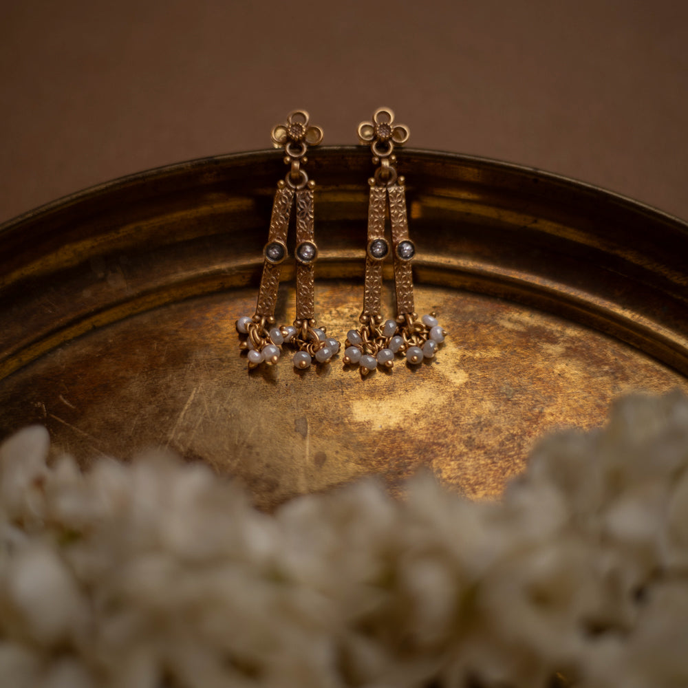 Antique gold drop earrings with white polki stones and pearl clusters, on a brass tray.