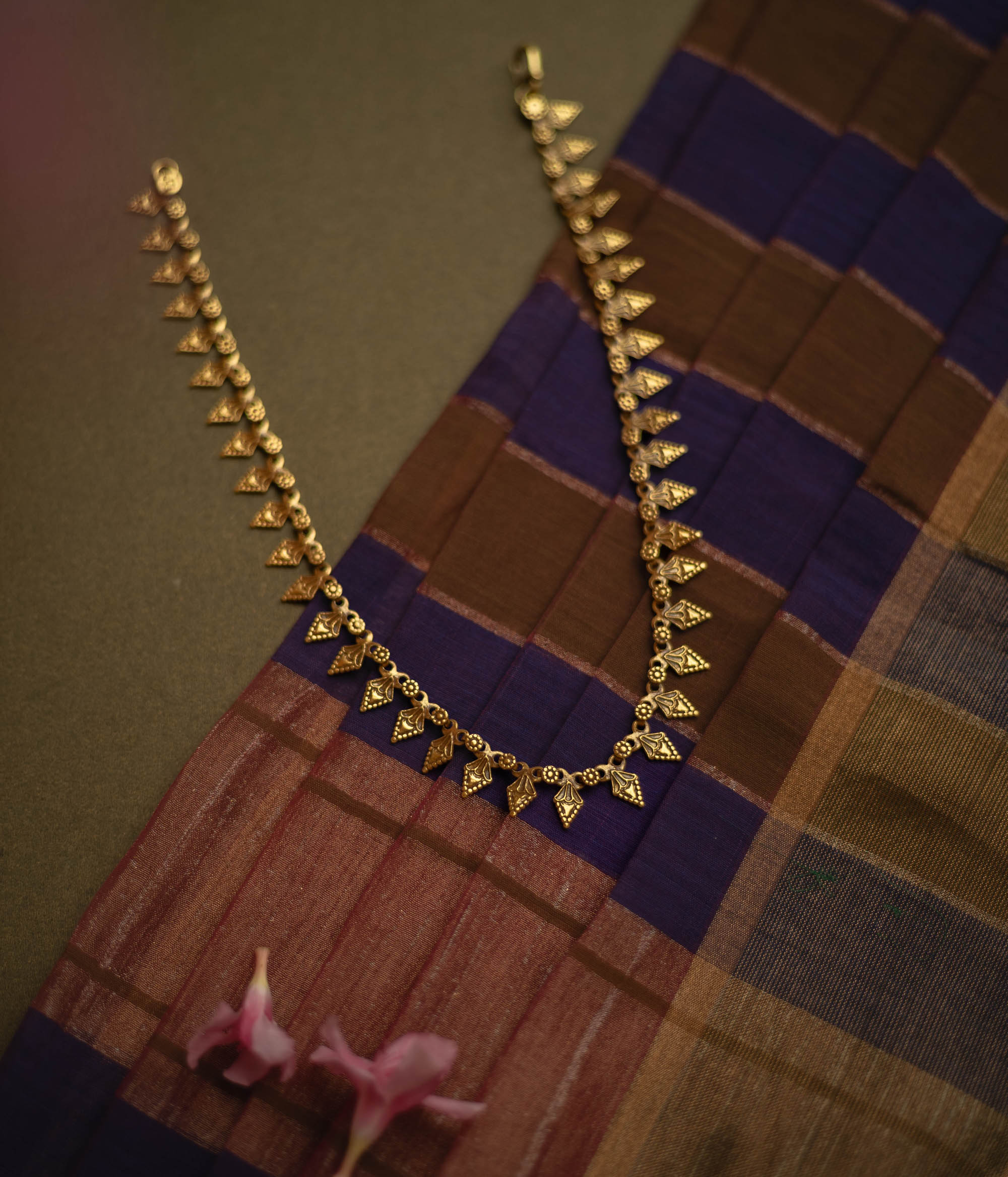 Gold tribal necklace with intricate leaf-like motifs, laid on a checkered fabric.