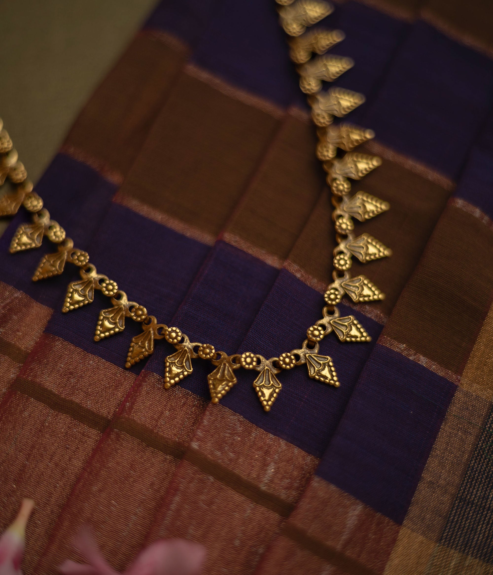 Gold tribal necklace with intricate leaf-like motifs, laid on a checkered fabric.
