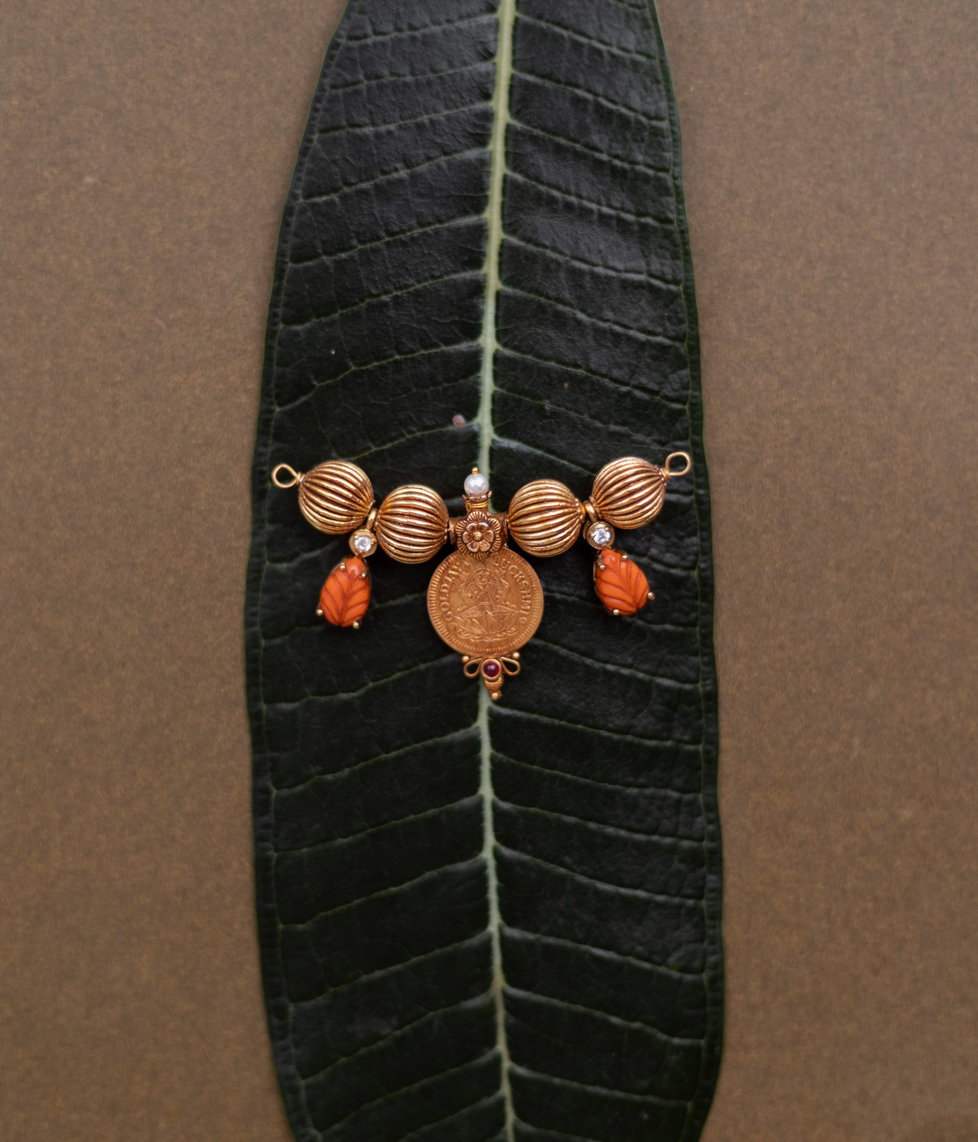 Traditional Mangalsutra pendant with Lakshmi coin, pearls, and red spinel stones on a leaf.