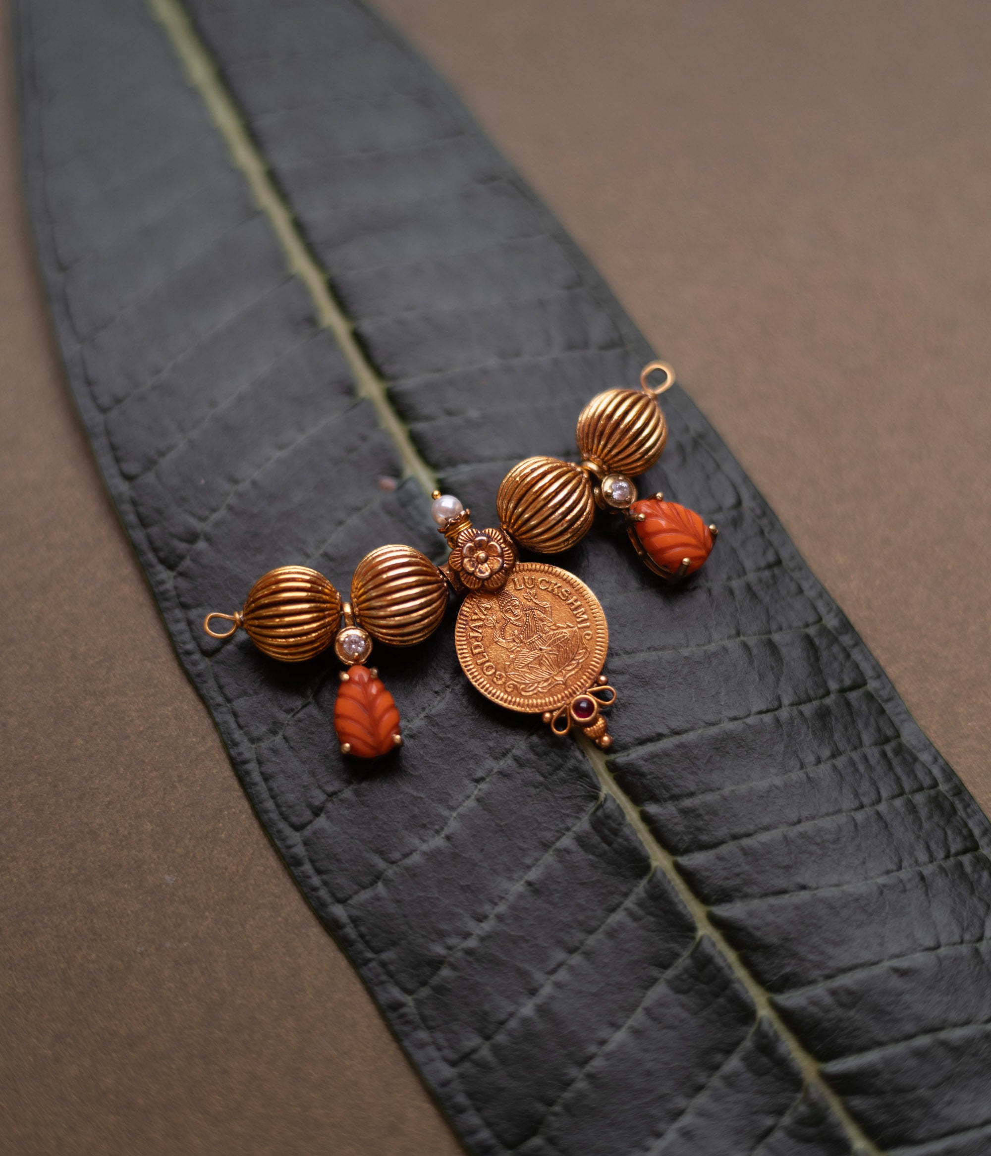 Traditional Mangalsutra pendant with Lakshmi coin, pearls, and red spinel stones on a leaf.