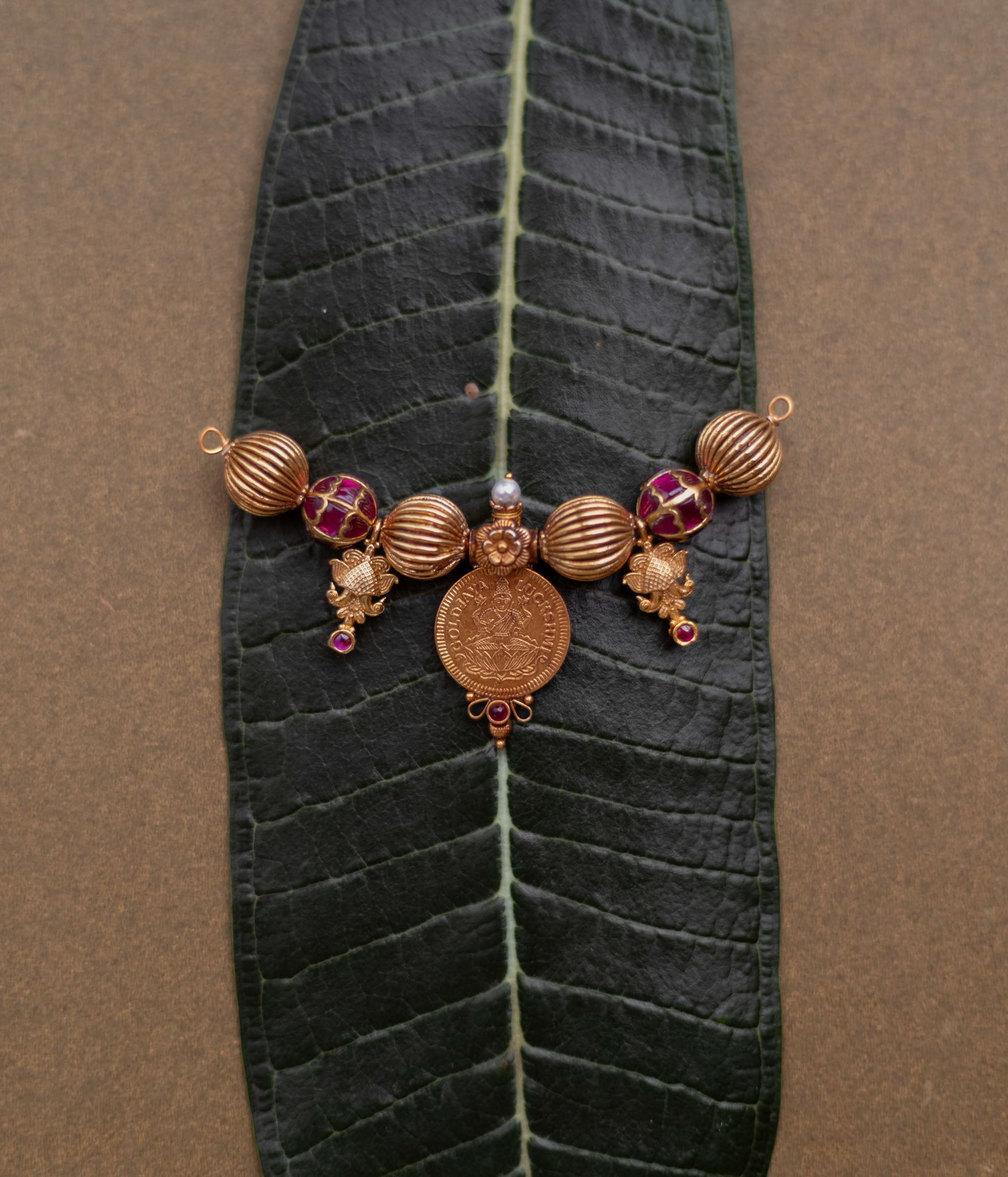 Antique Mangalsutra pendant with Lakshmi coin, red spinel stones, pearls, and floral detailing.