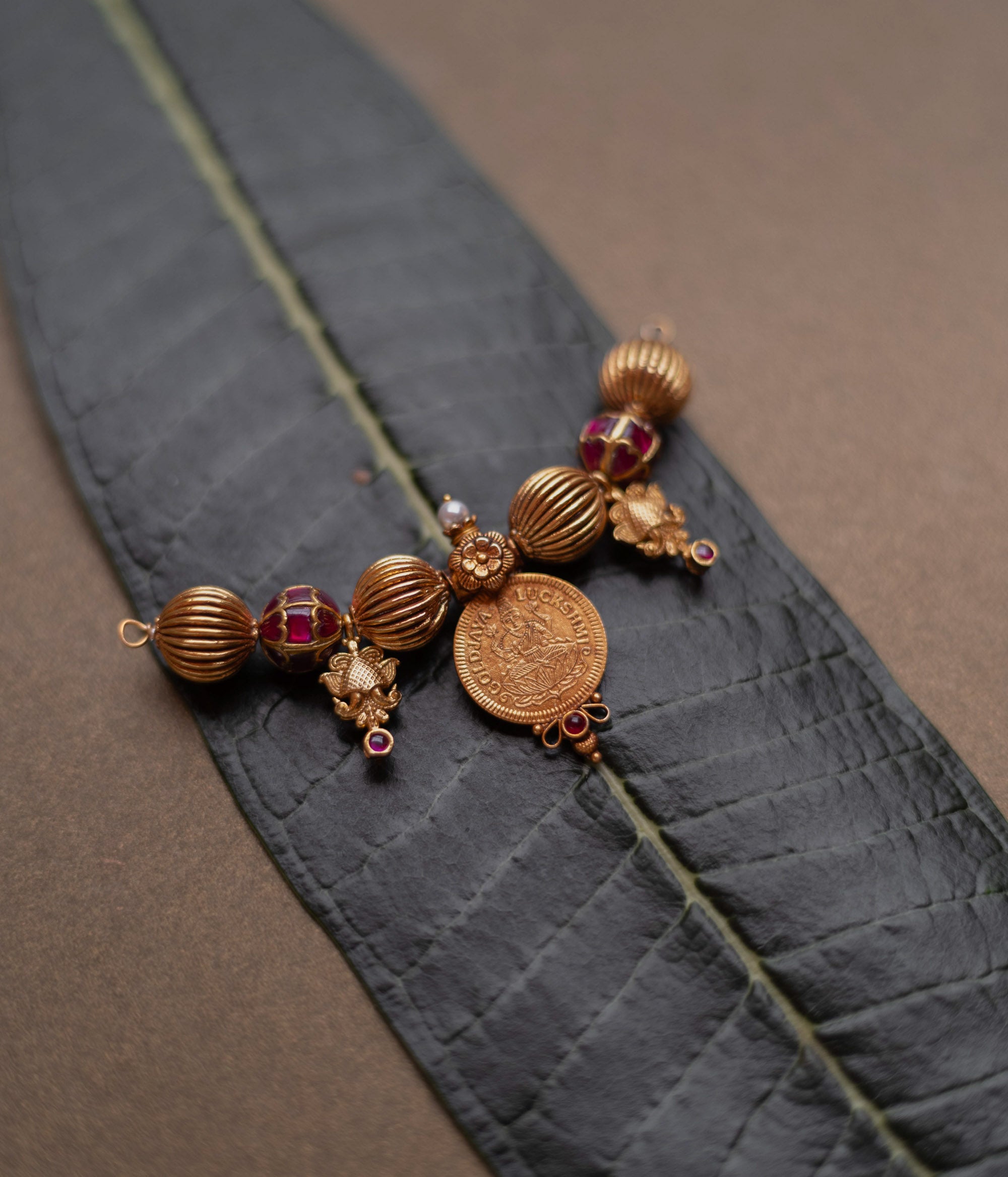 Antique Mangalsutra pendant with Lakshmi coin, red spinel stones, pearls, and floral detailing.